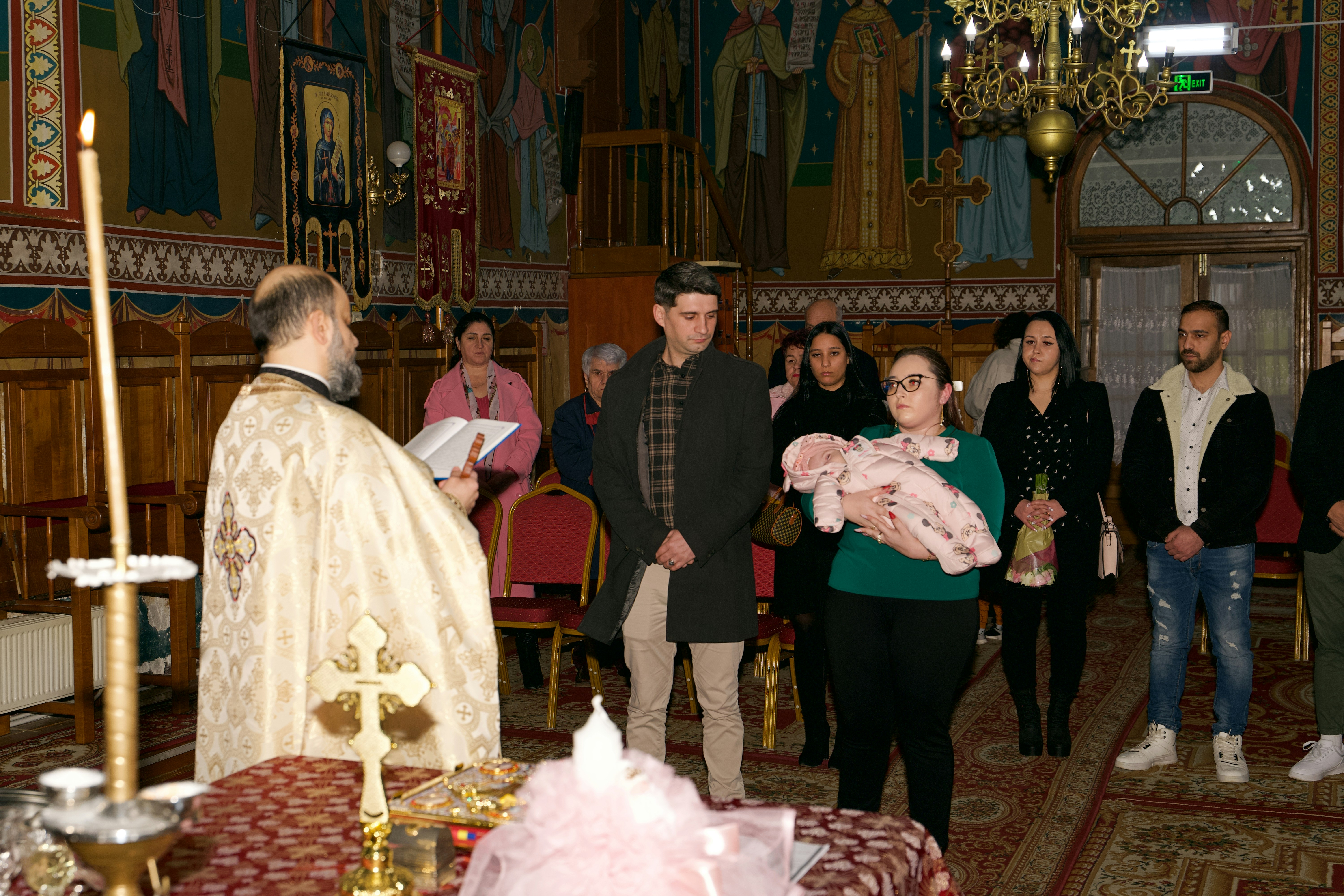 A priest officiating a baptism ceremony for a baby held by a woman