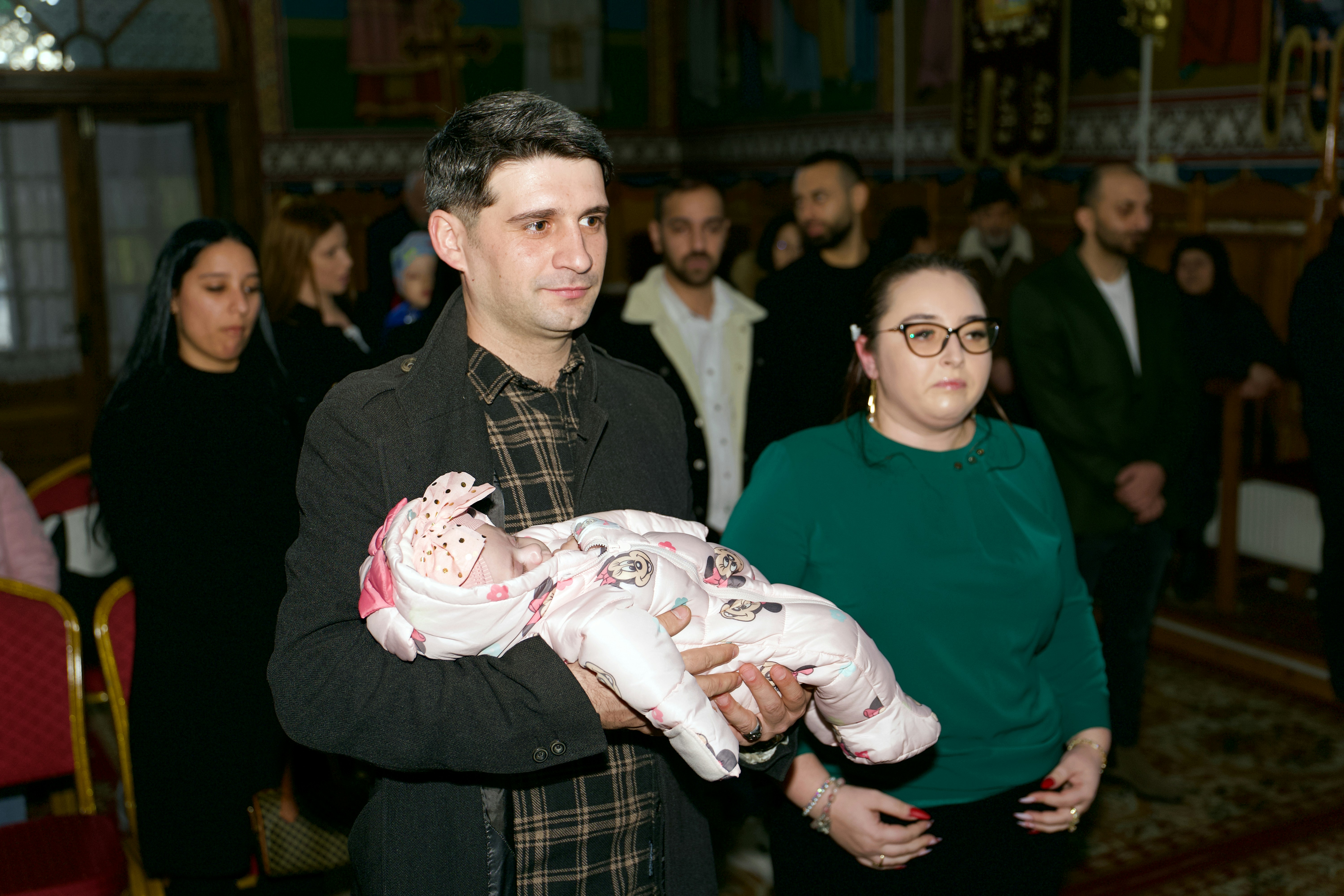 A man holding a baby in a pink snowsuit inside a church