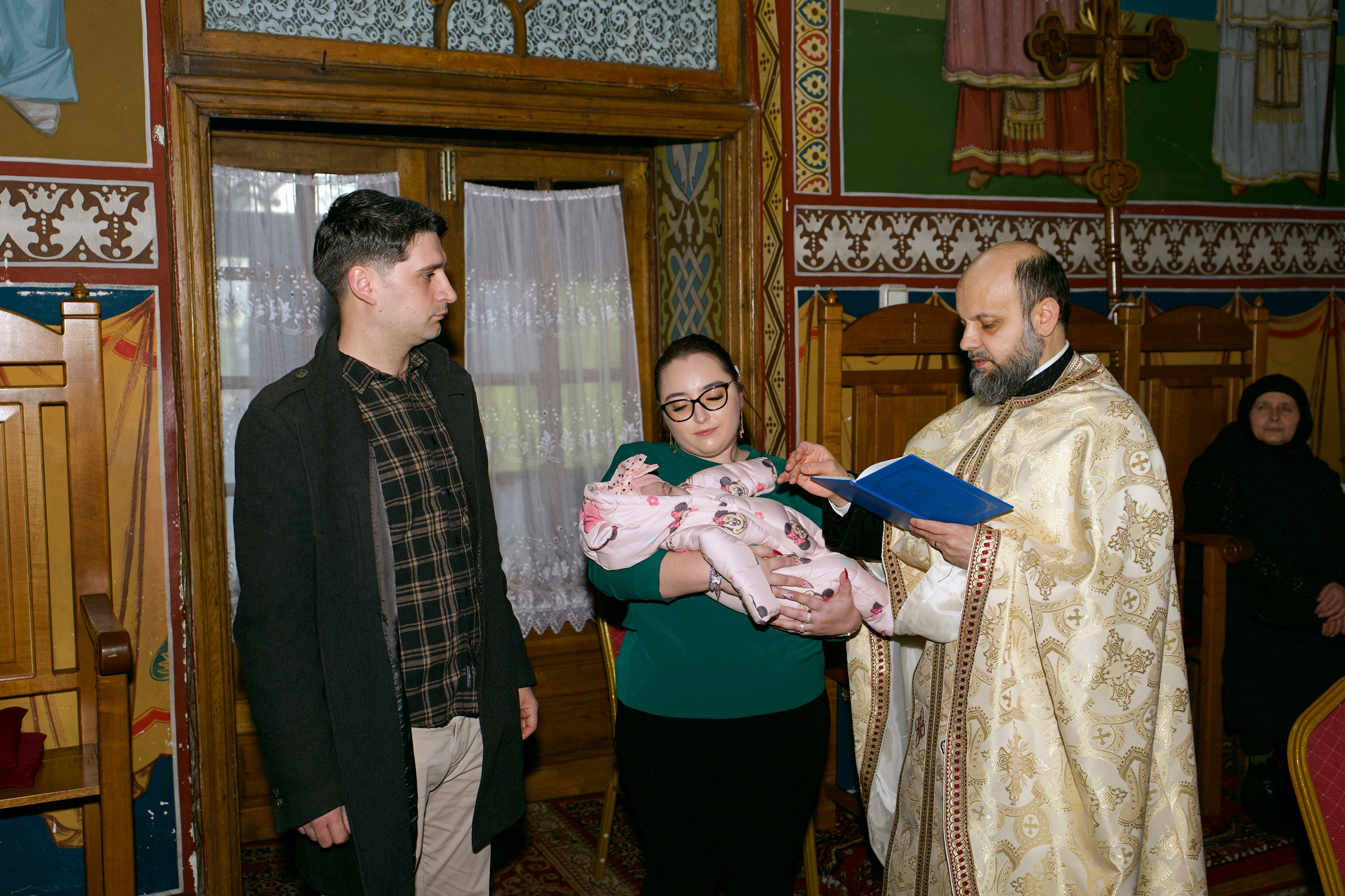 A priest in ornate vestments reading from a book during a baptism ceremony