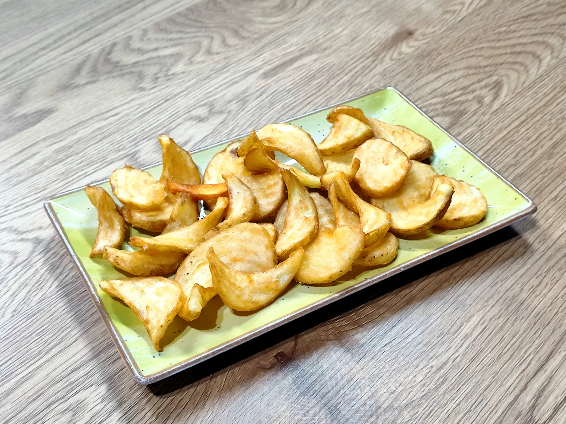 A pile of golden, crisp potato slices on a light green rectangular plate