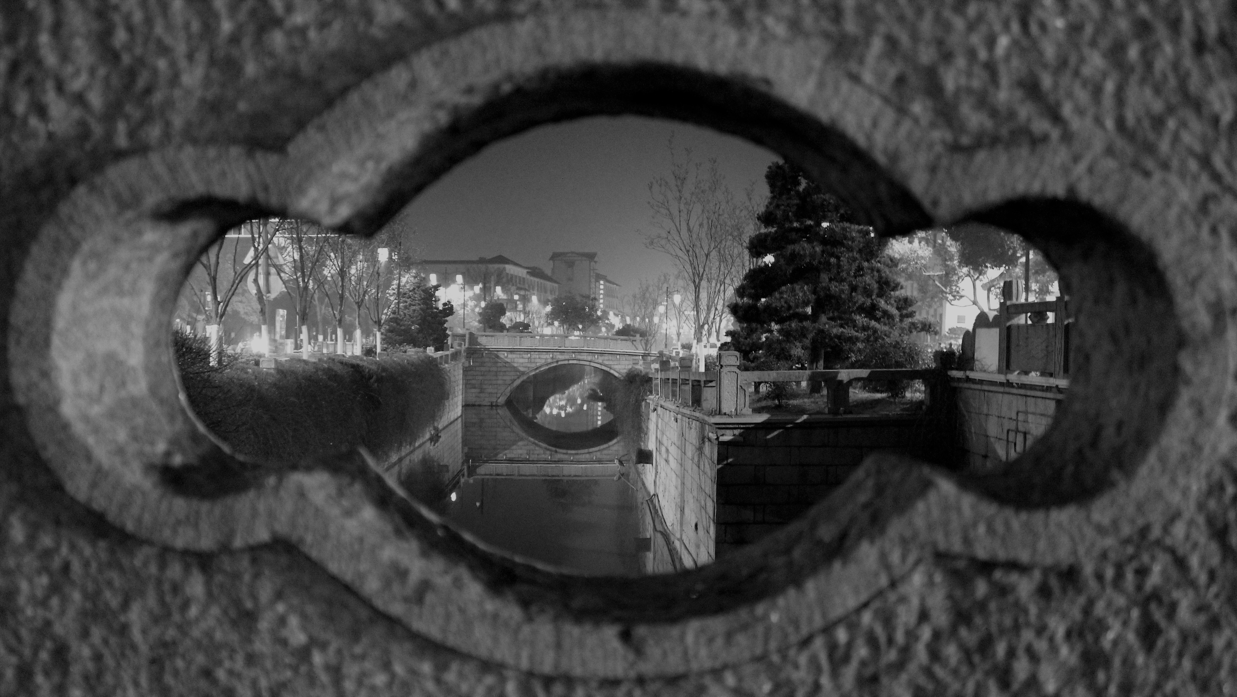 A stone bridge over a canal at night viewed through a decorative opening