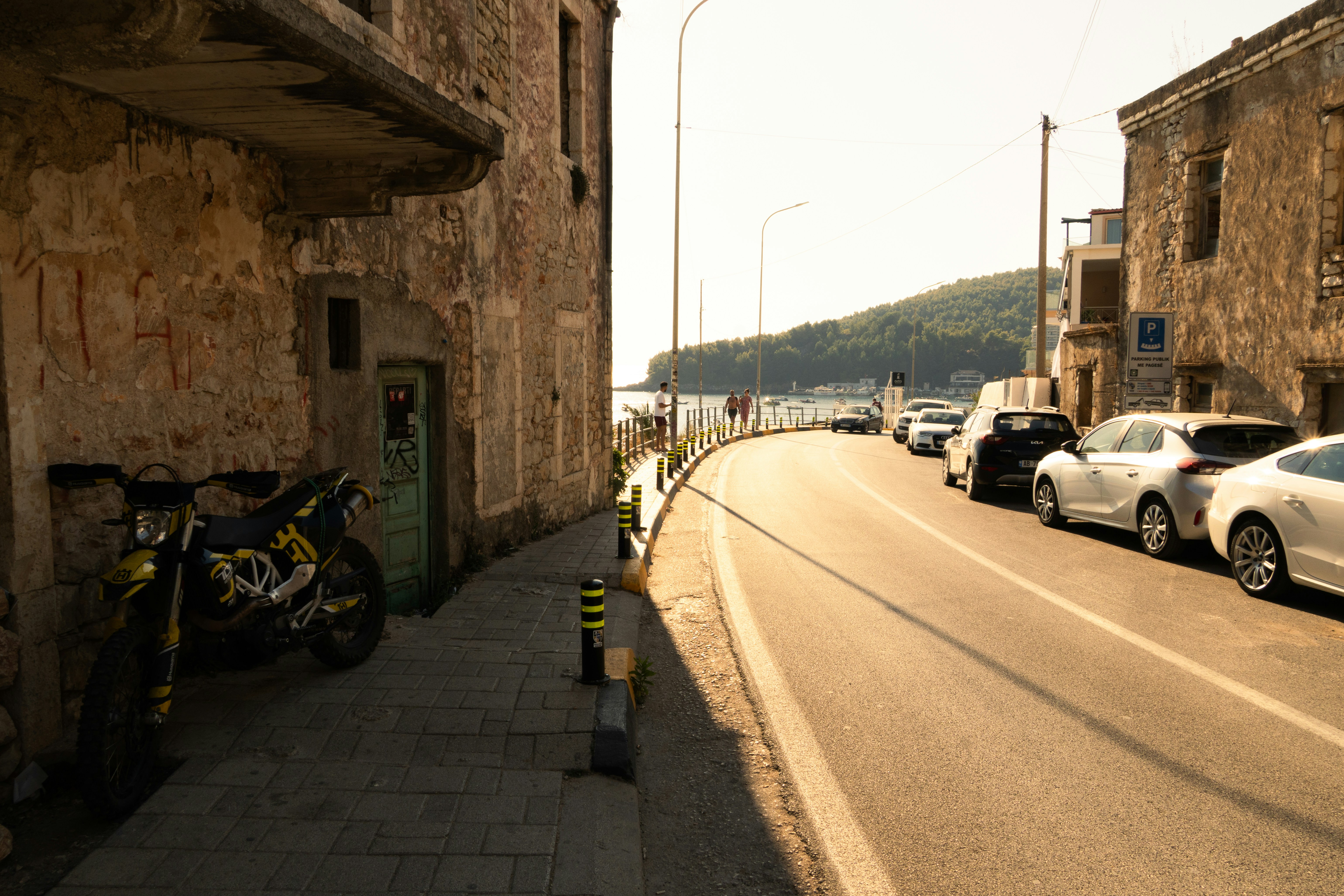 A motorcycle parked on a stone sidewalk beside a road with parked cars