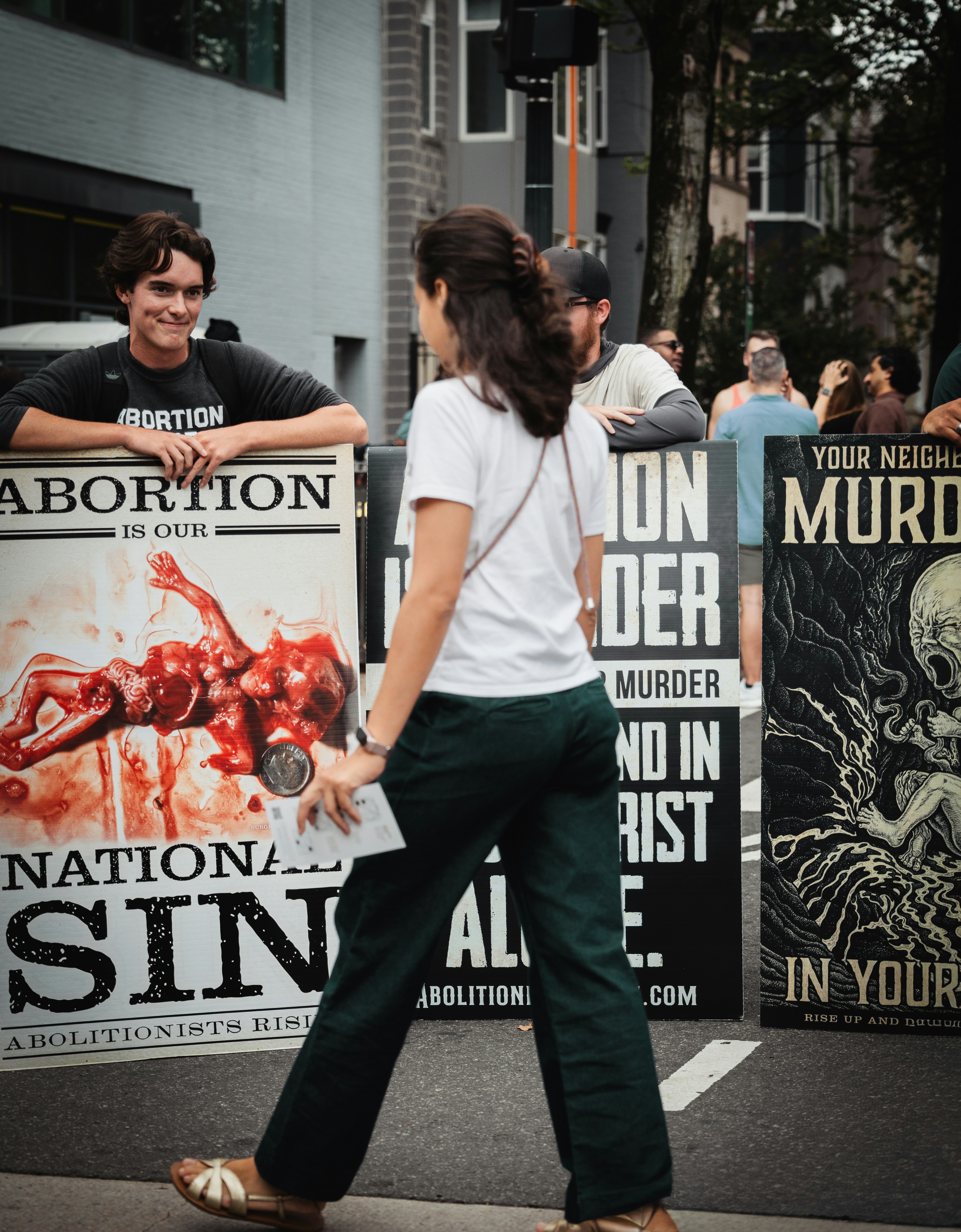 A person walking past people holding signs with graphic illustrations on a city street
