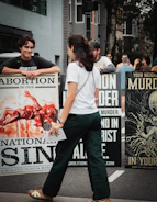 A person walking past people holding signs with graphic illustrations on a city street