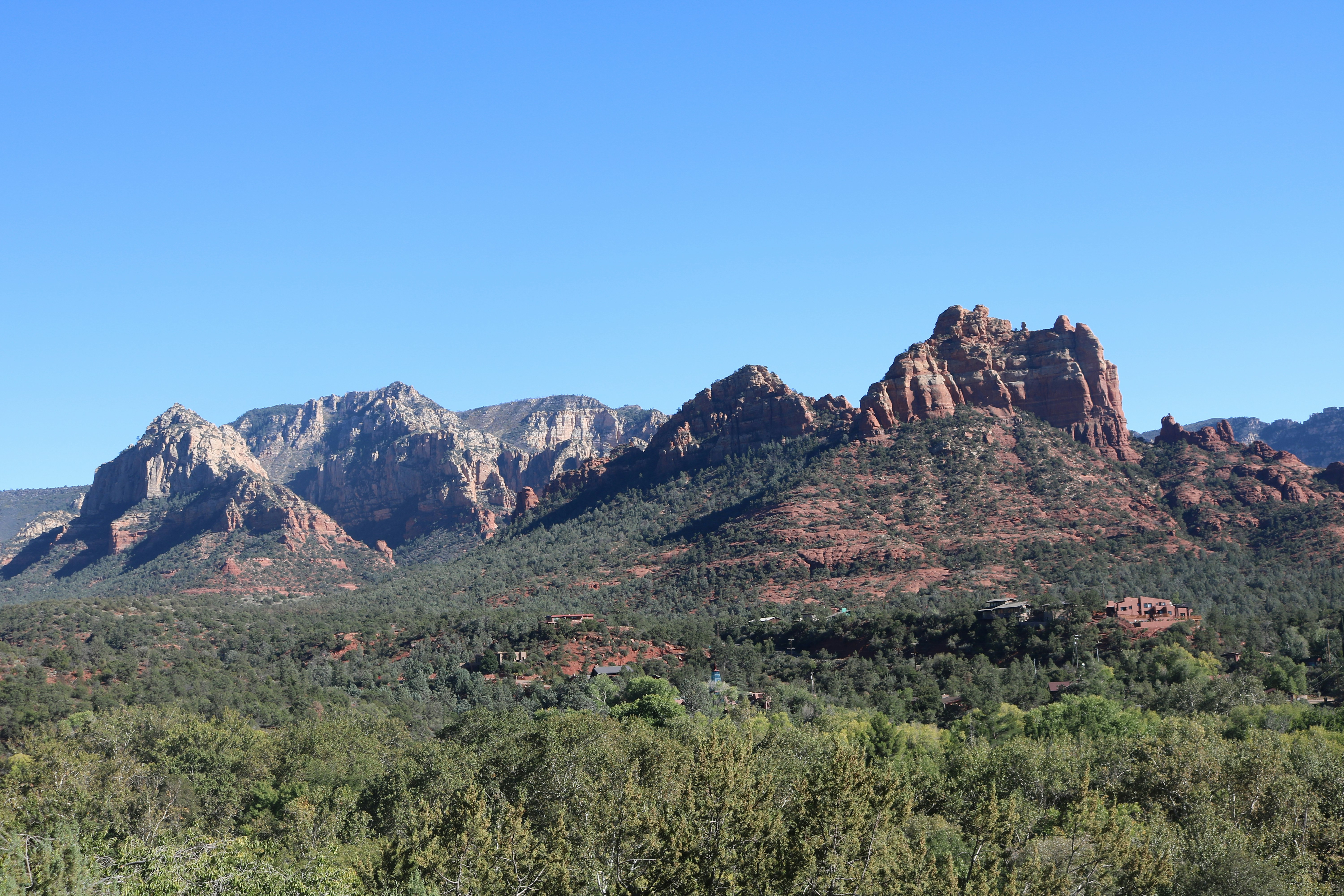 Red rock formations rising above a green forest under a clear blue sky