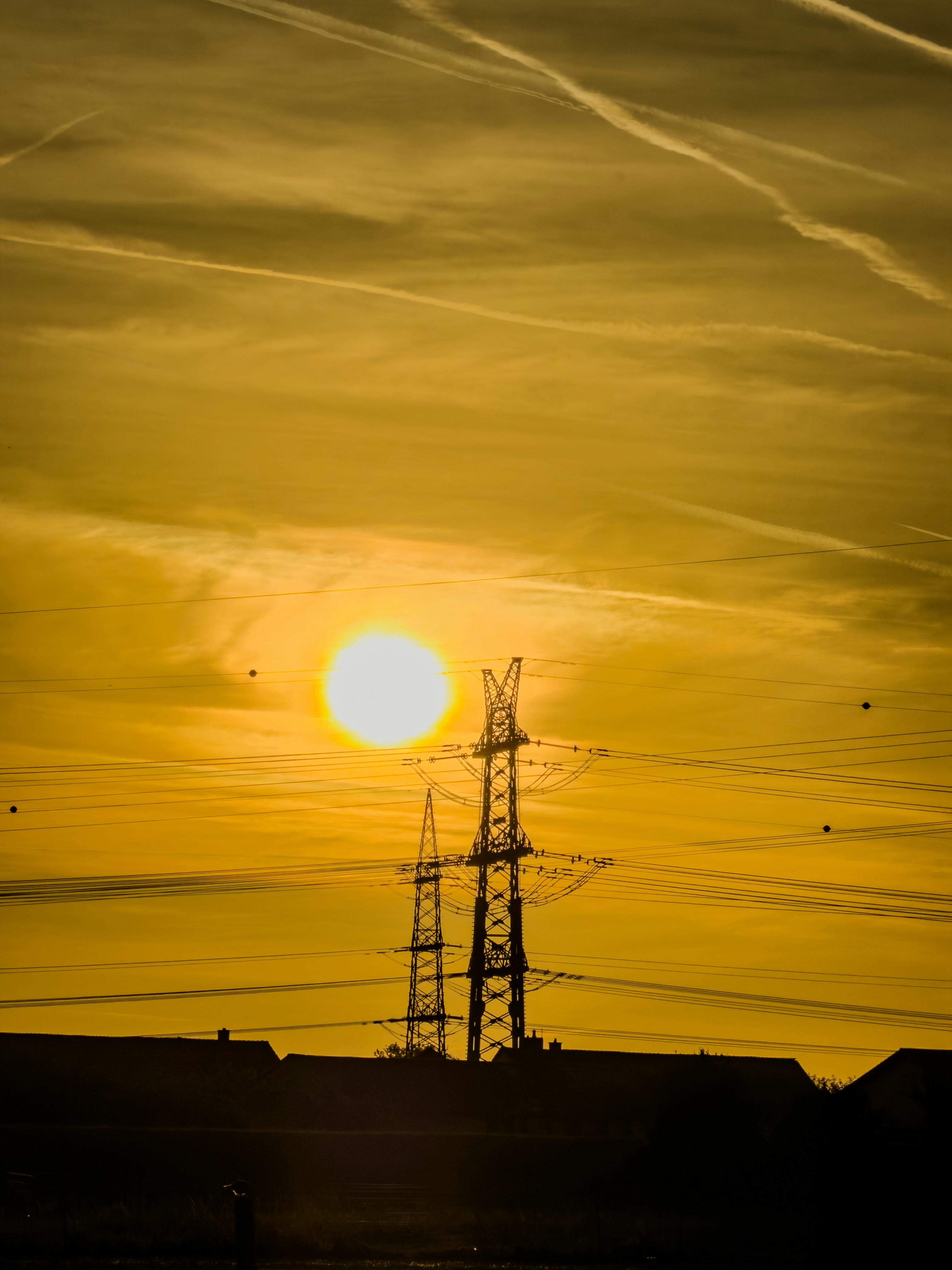 Electricity pylons in silhouette against a bright yellow sky with low sun