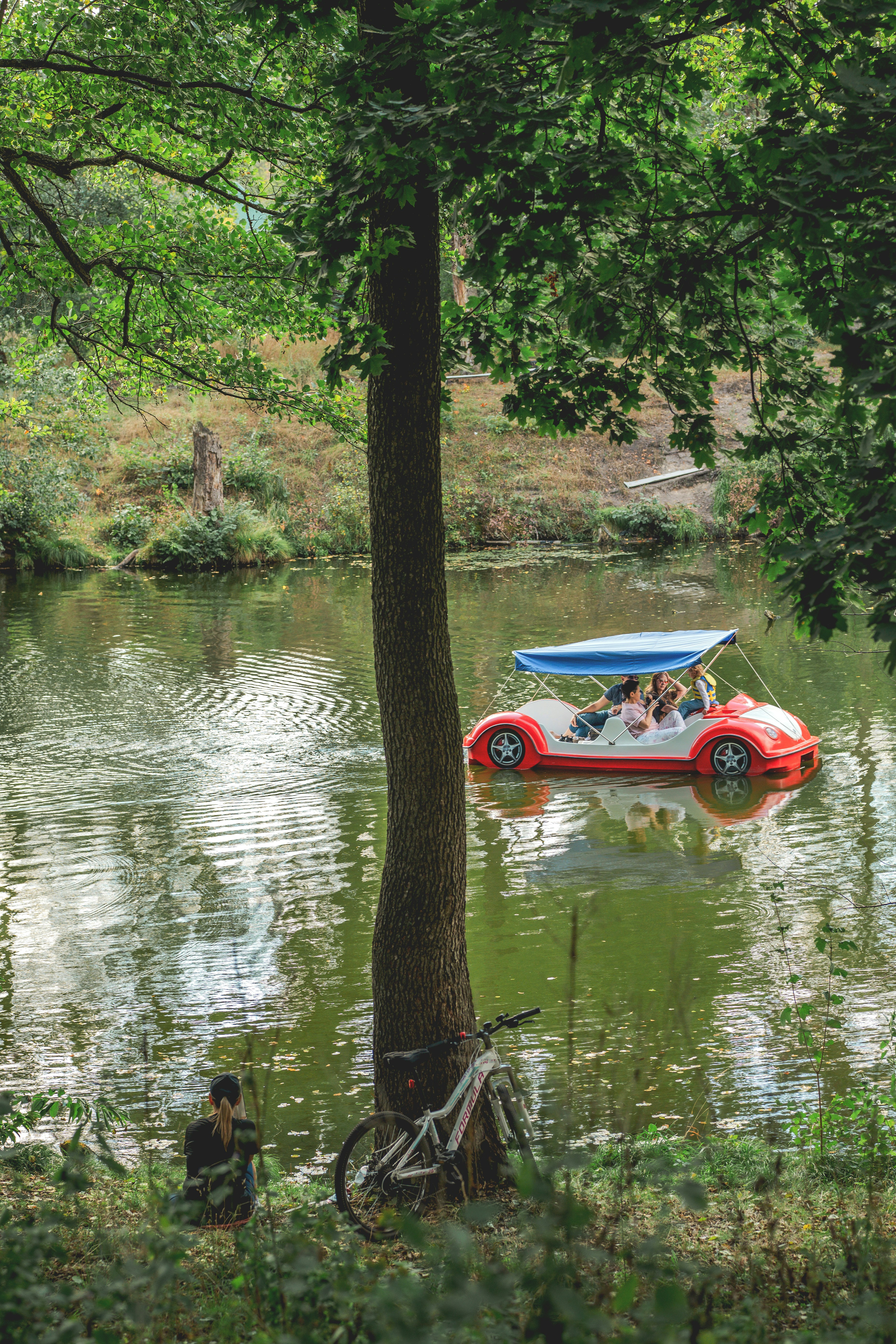 A red pedal boat with a blue canopy on a calm lake