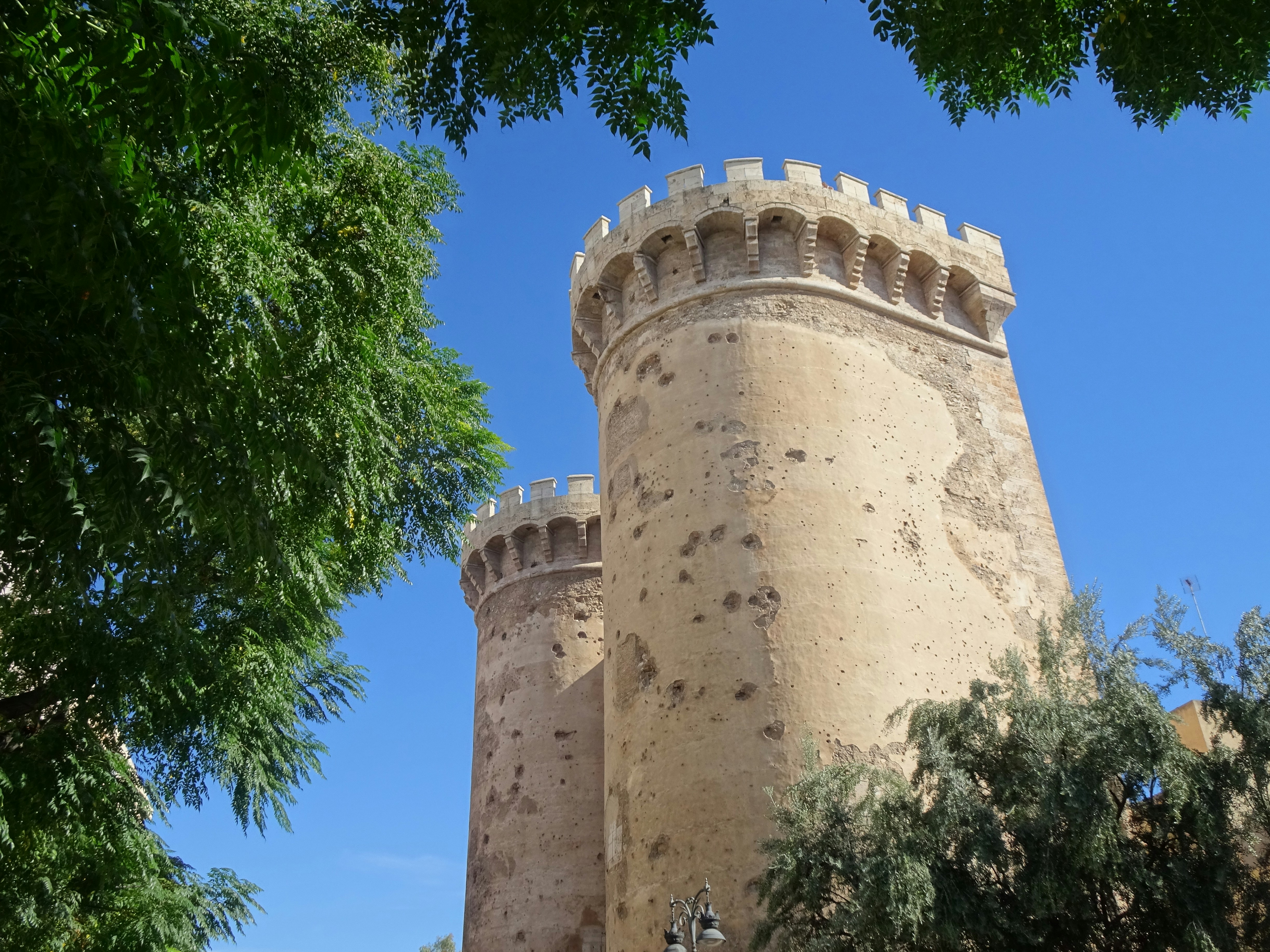 Two stone towers of the Serranos Towers in Valencia framed by green trees