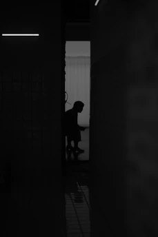 A person in silhouette against a bright doorway in a dark tiled room