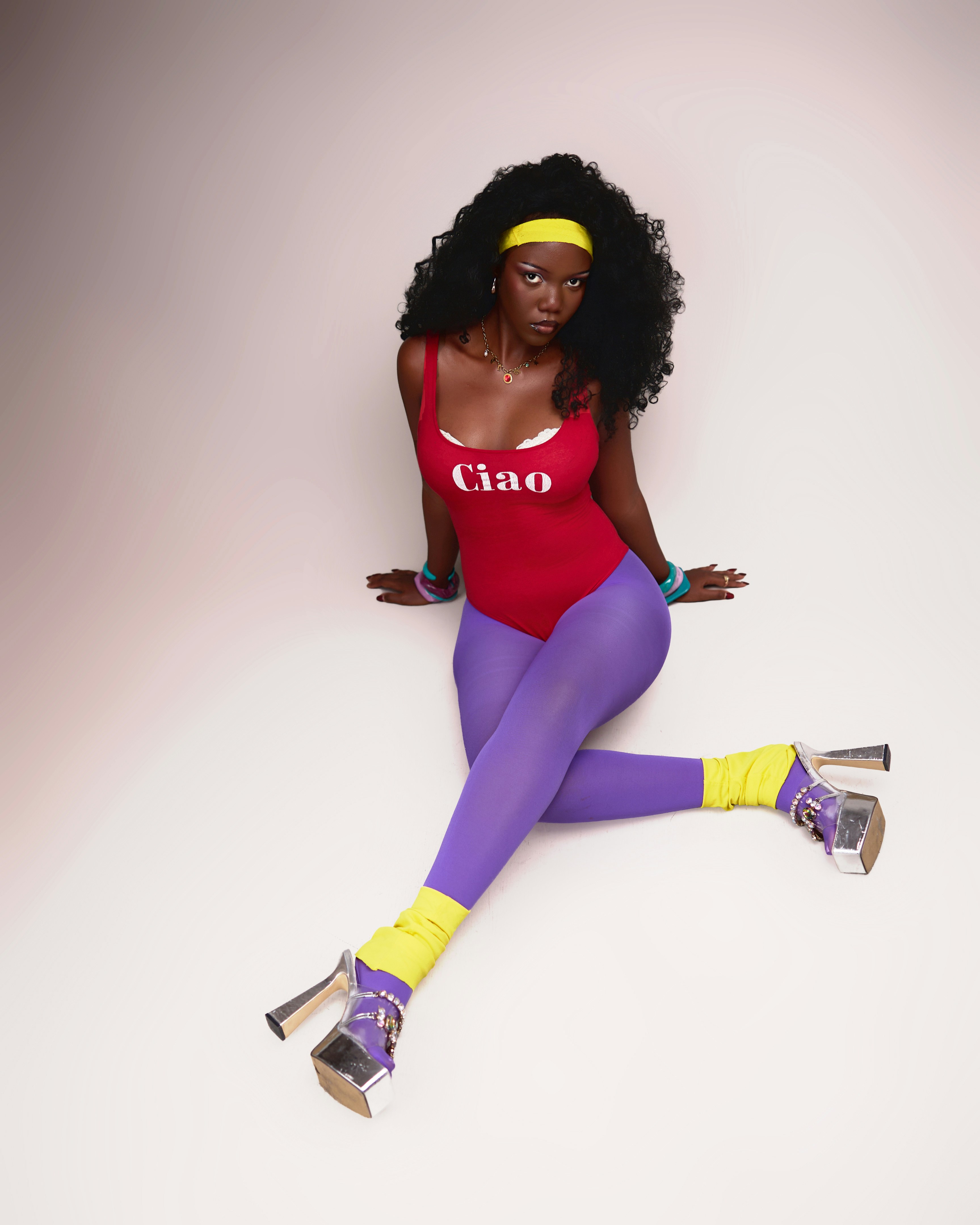 A woman in a red Ciao bodysuit and purple leggings with yellow leg warmers