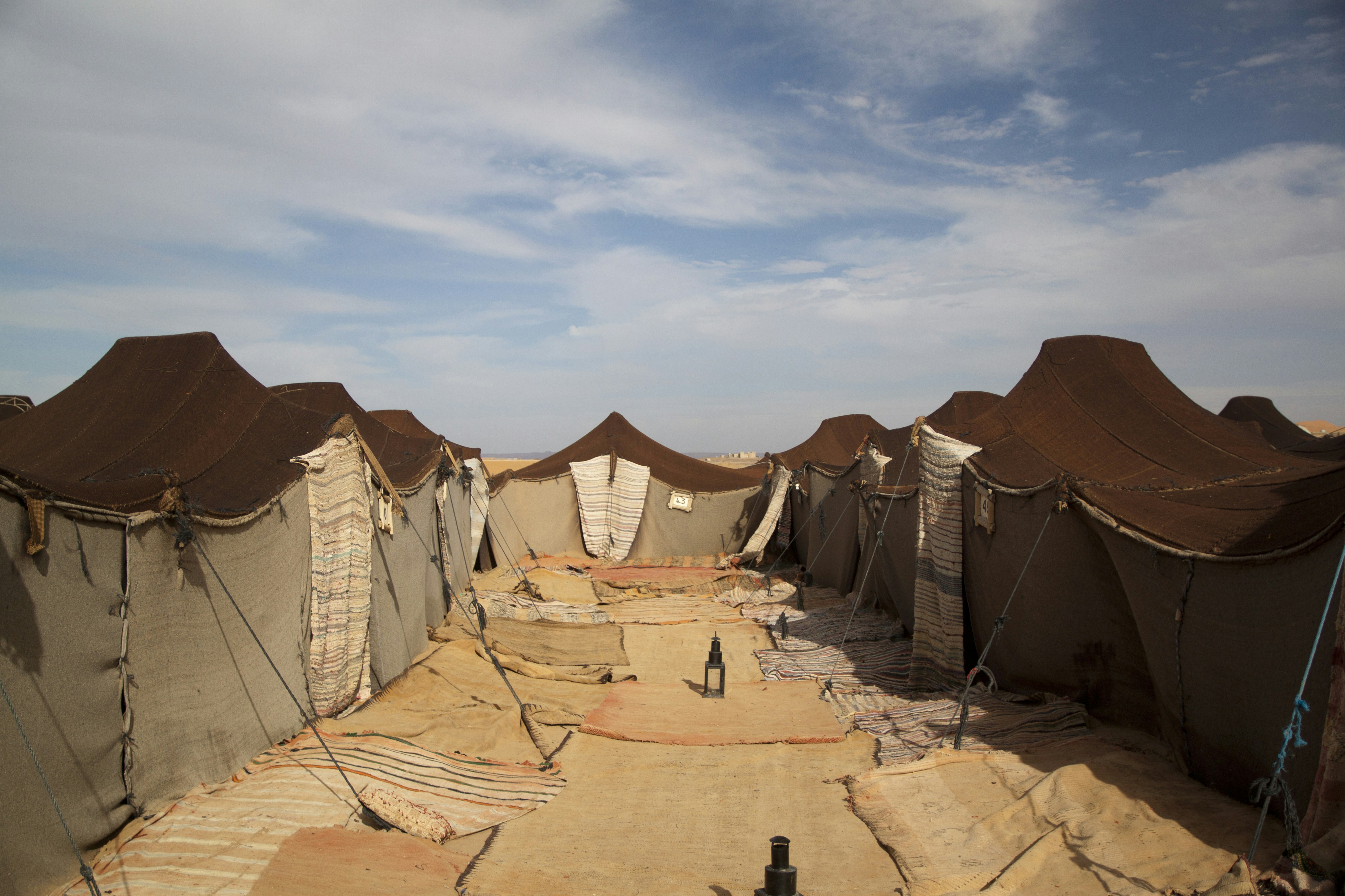 A row of brown Bedouin tents in a desert under a blue sky
