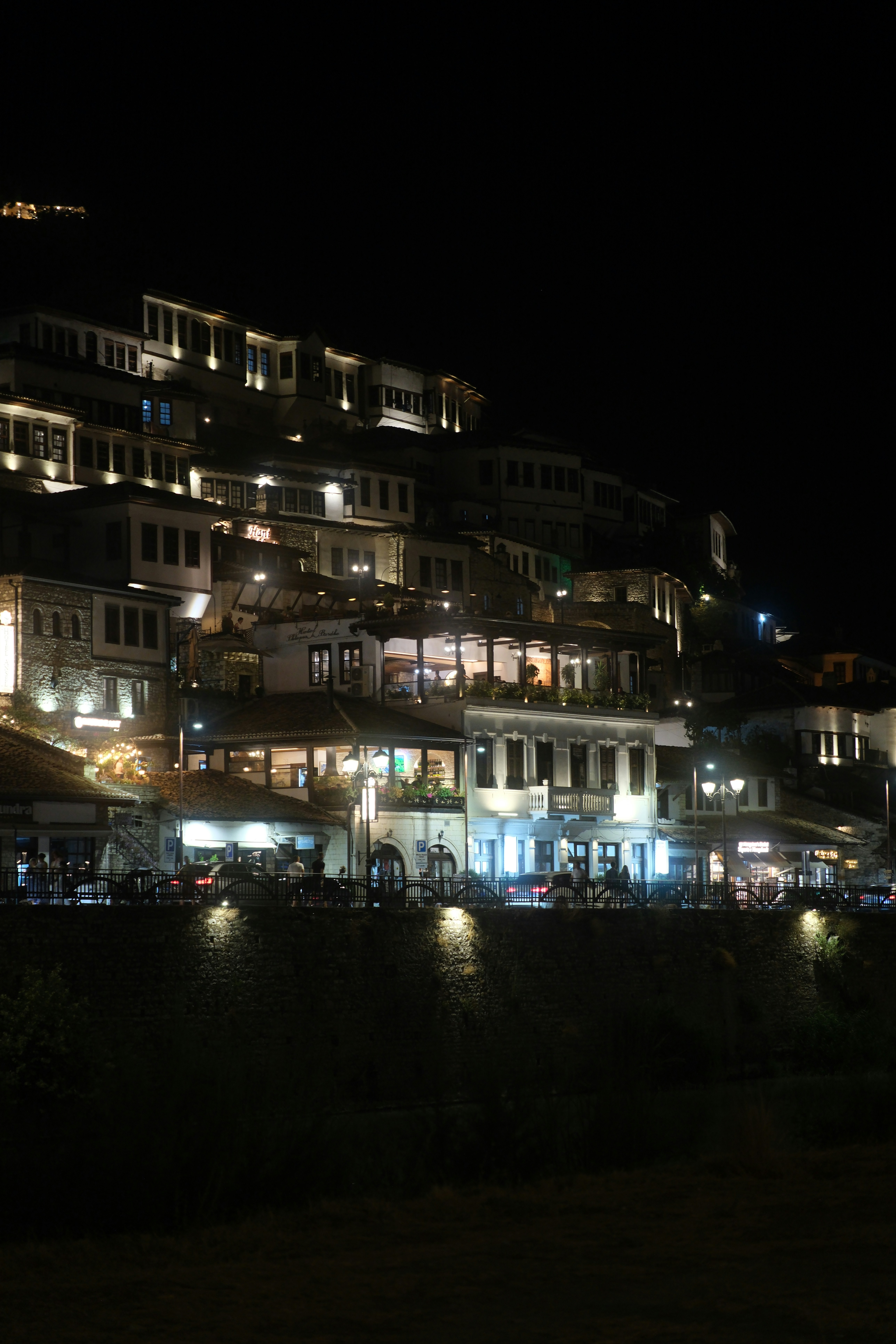 Illuminated white houses stacked on a hillside at night in Berat, Albania