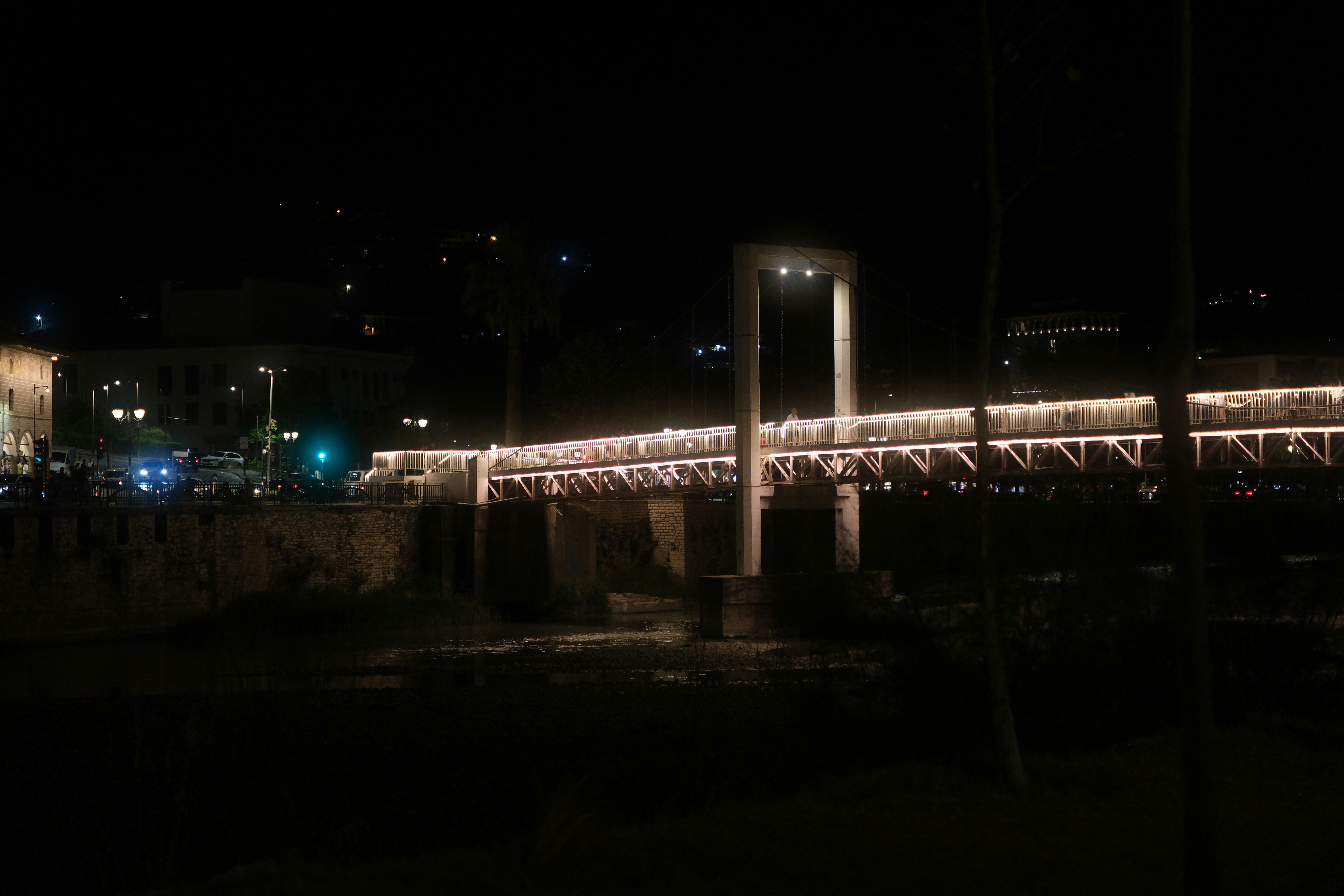 A pedestrian bridge illuminated by warm lights at night over a dark river