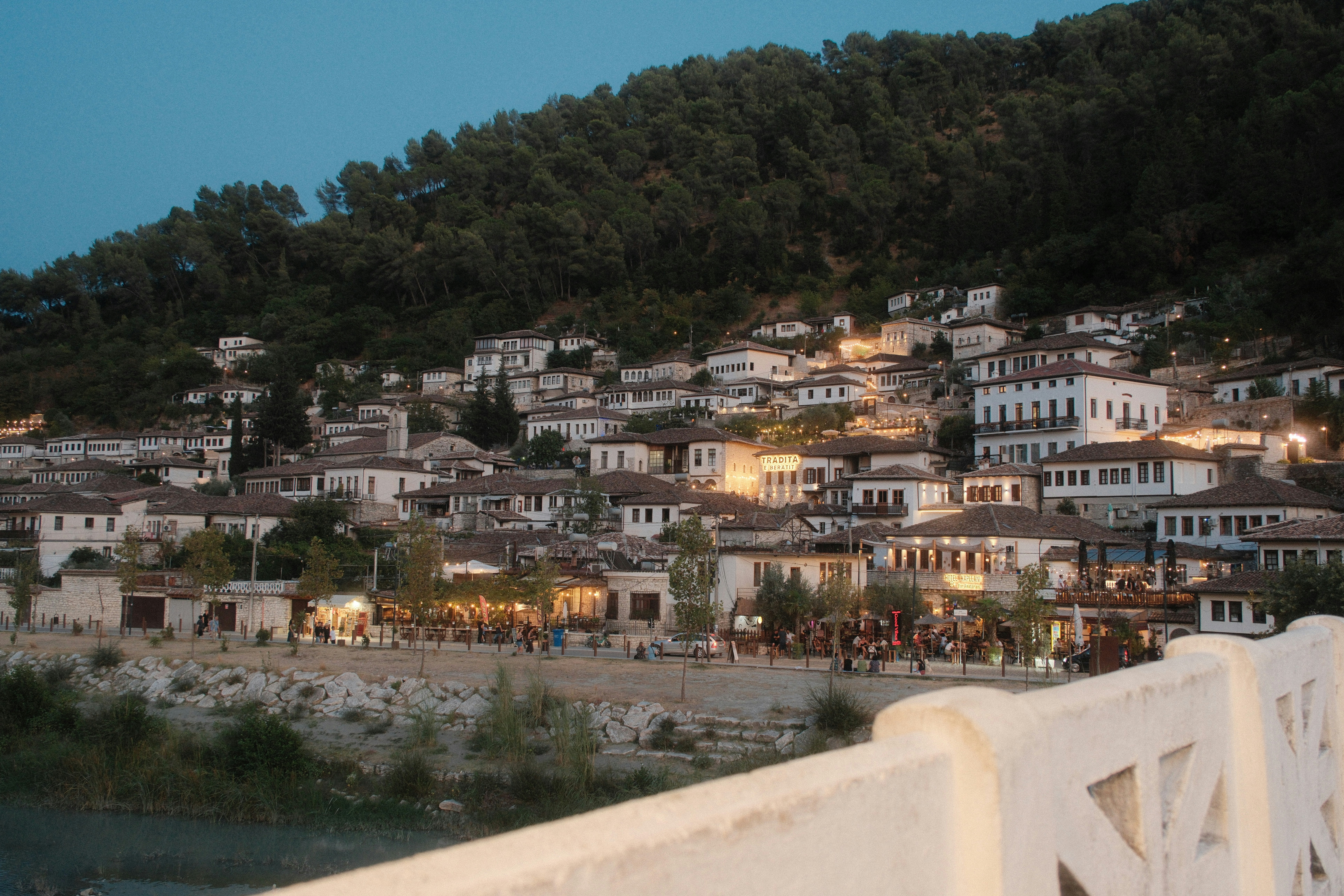 White houses with brown roofs on a hillside above a river in Berat