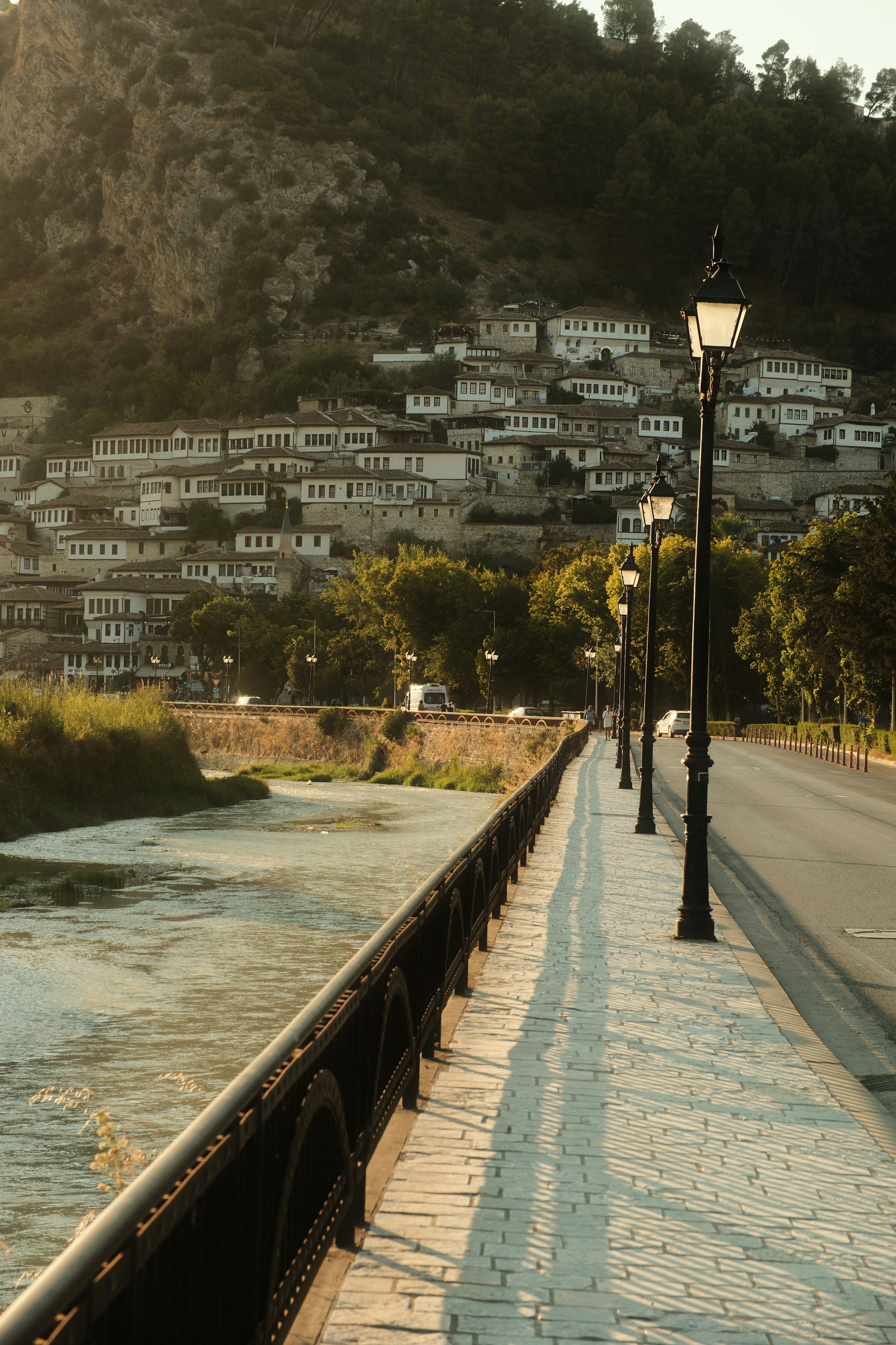 A riverside road with ornate street lamps beside white houses in Berat, Albania