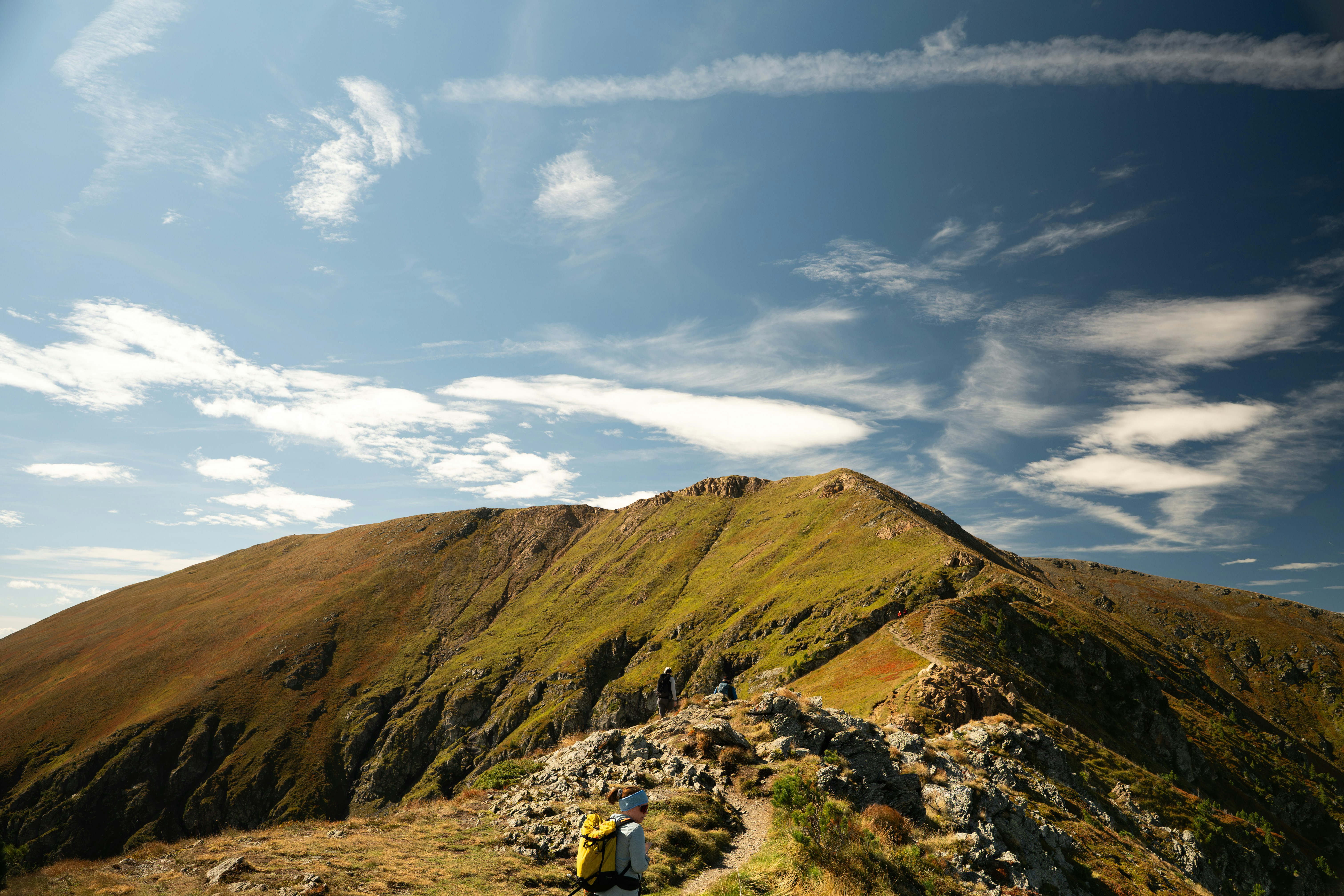 Hikers on a rocky mountain trail under a blue sky with wispy clouds