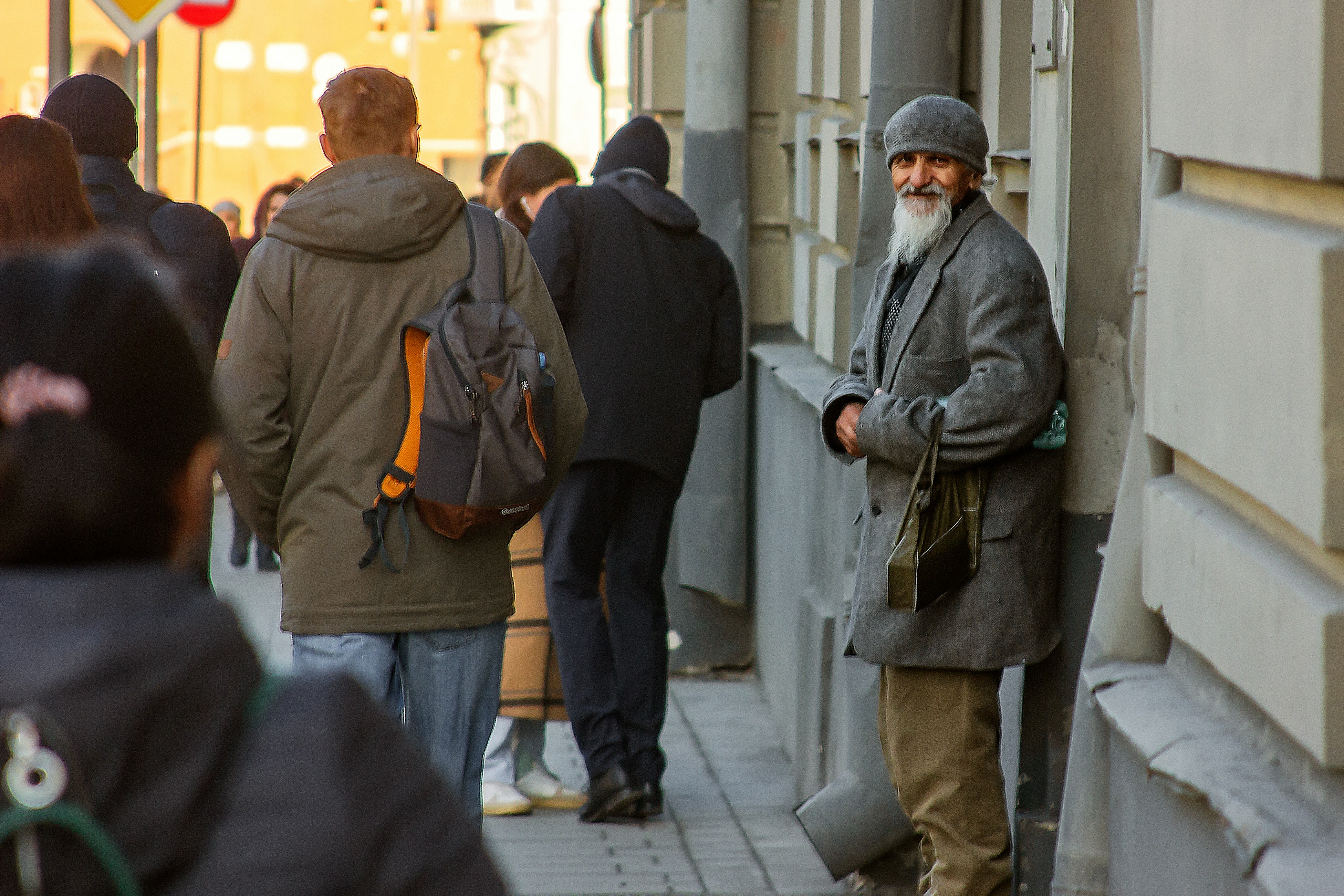 Un uomo anziano con la barba bianca e un cappotto grigio su un marciapiede cittadino