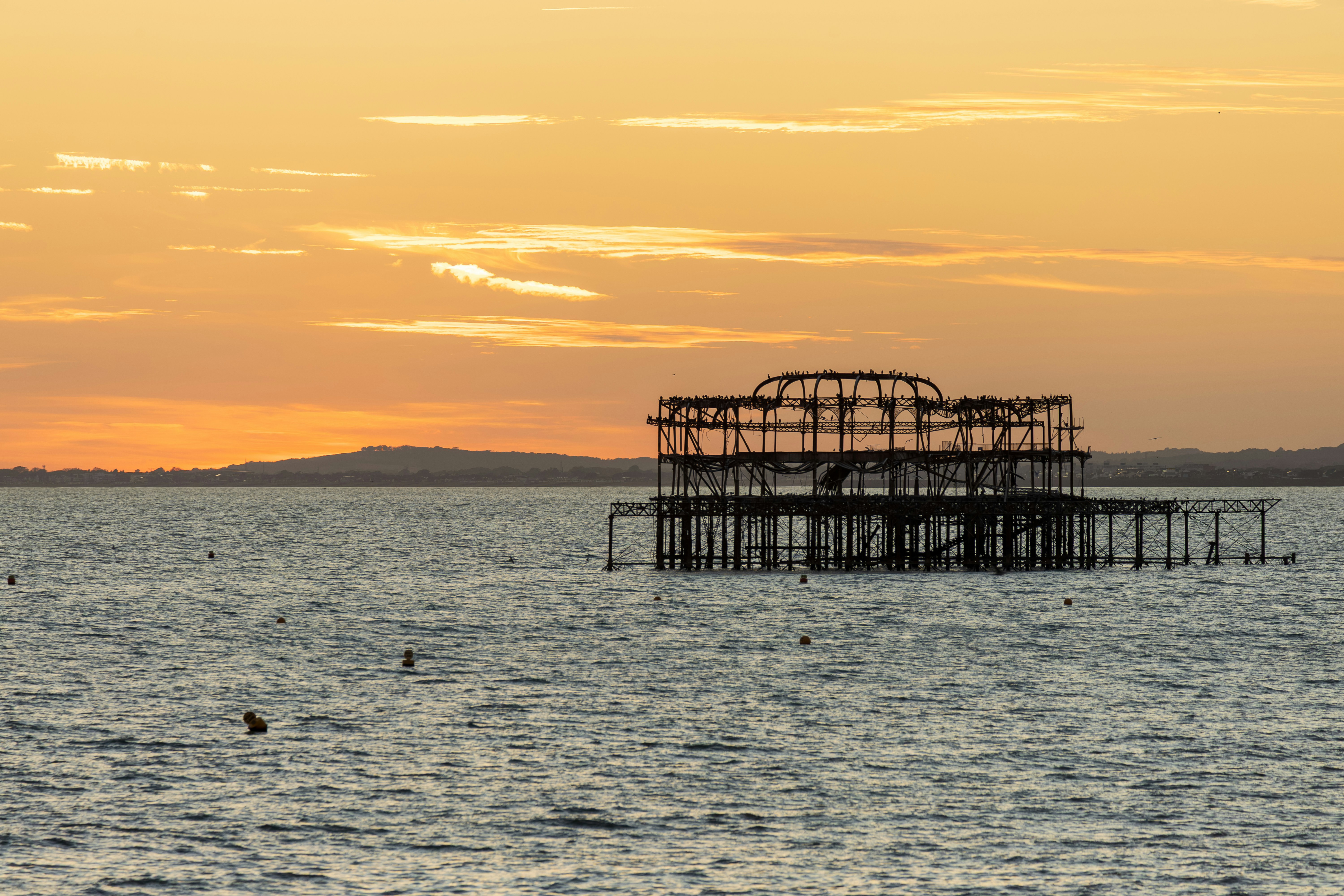 The skeletal remains of the West Pier in Brighton against a warm orange sky