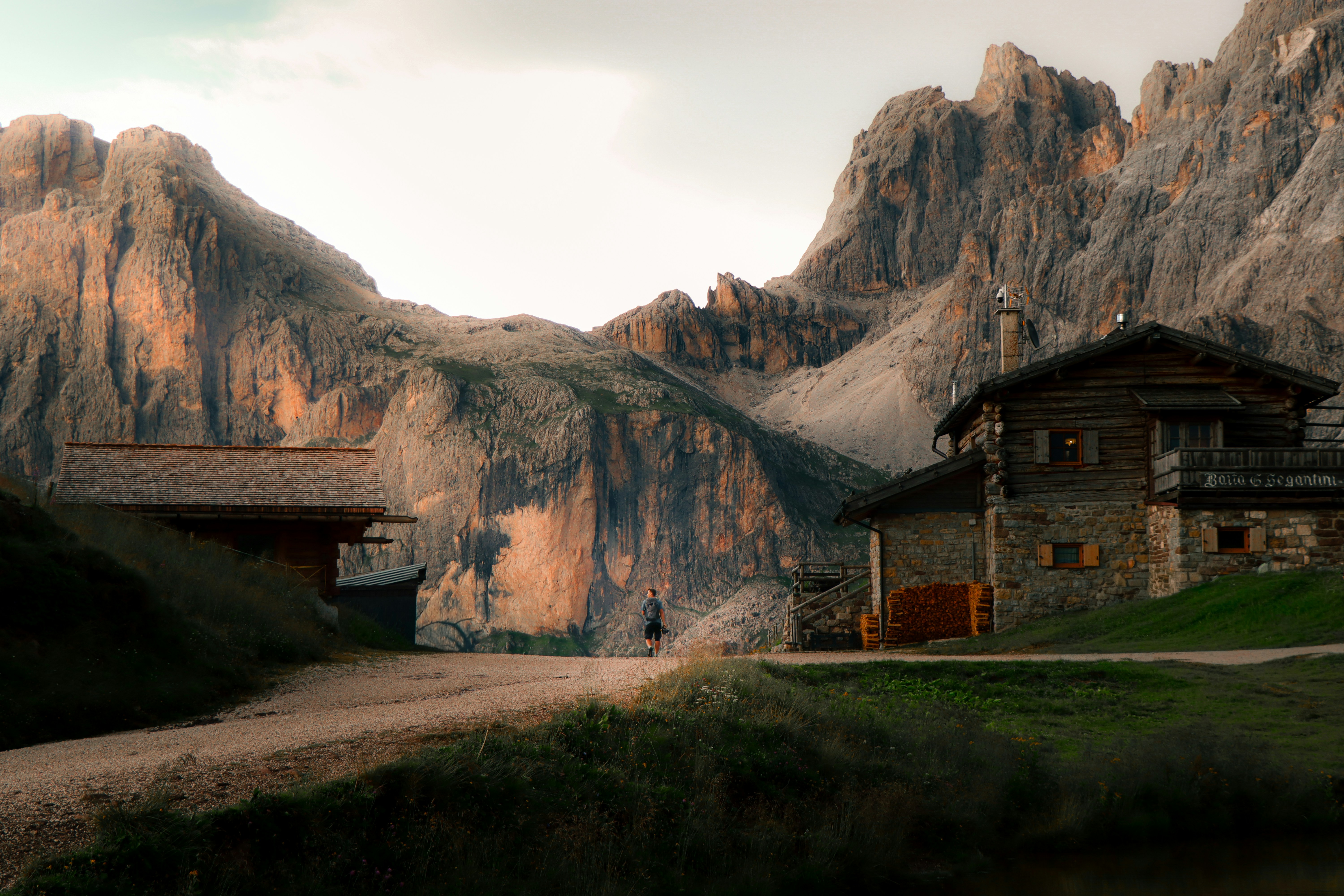 A person walking on a dirt path between two rustic wooden cabins in the mountains