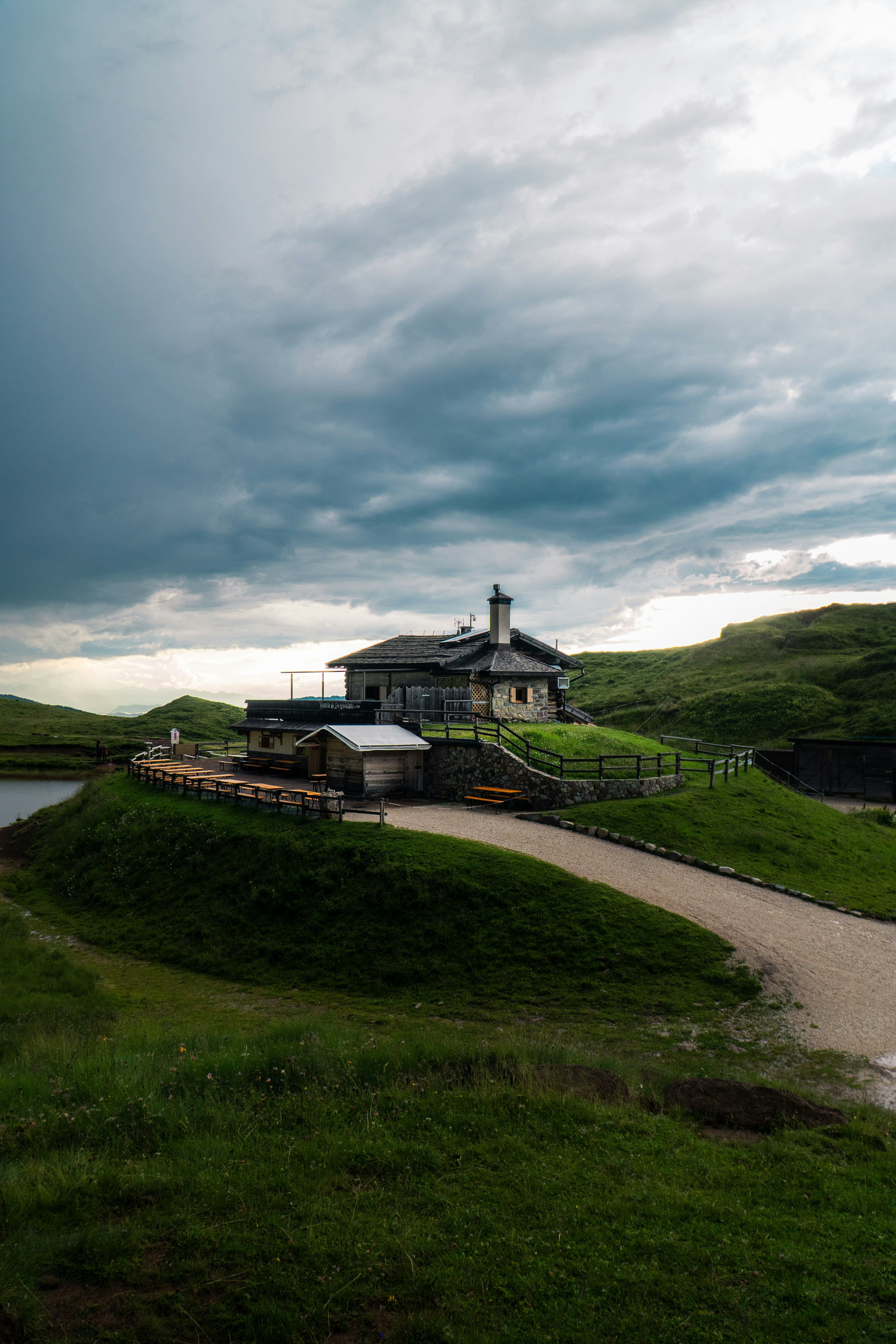 A stone mountain hut with a wooden roof on a grassy hill under cloudy skies