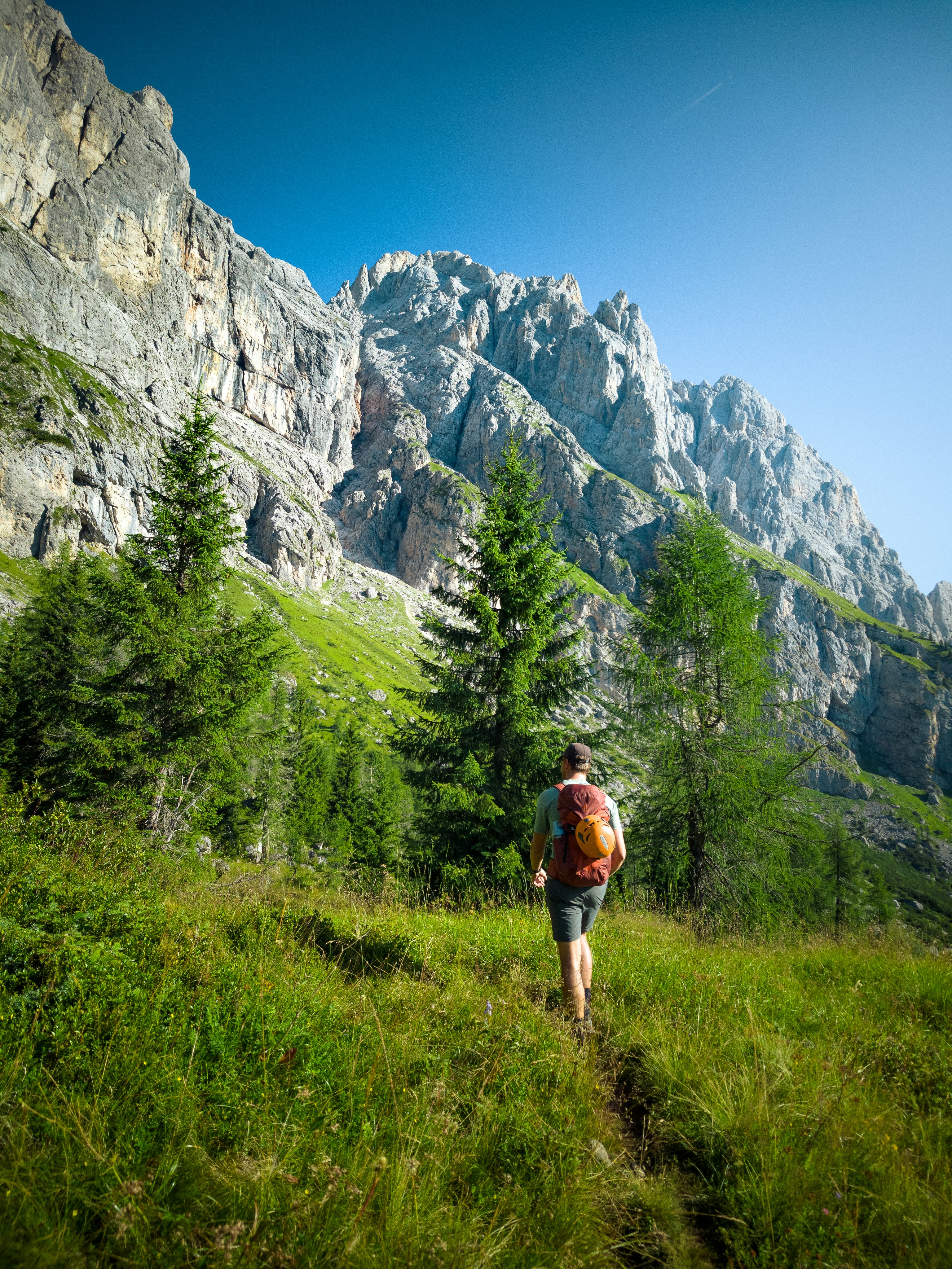 A hiker with a backpack and helmet walking on a trail in the mountains