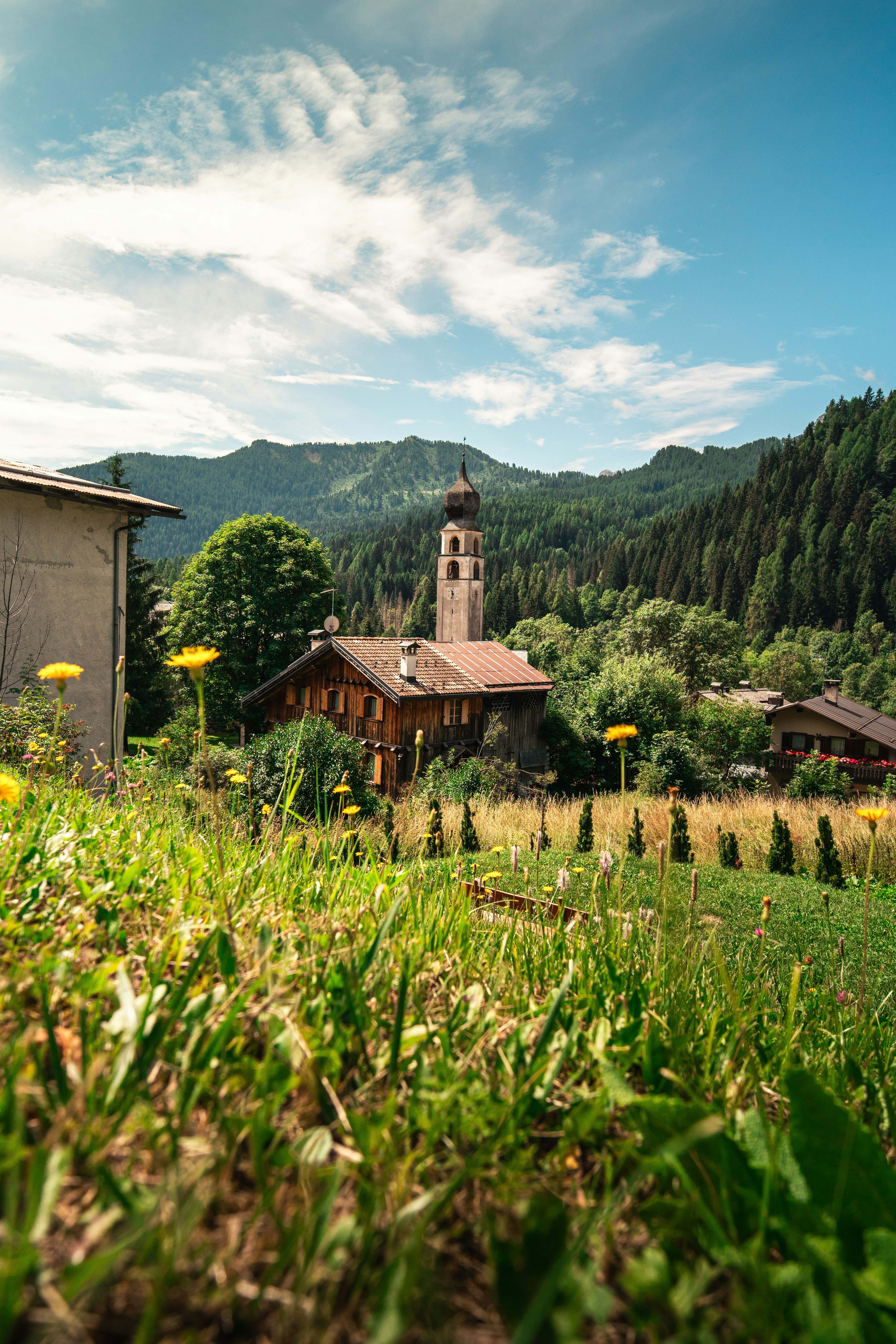 A church tower and wooden houses in a green valley with mountain slopes