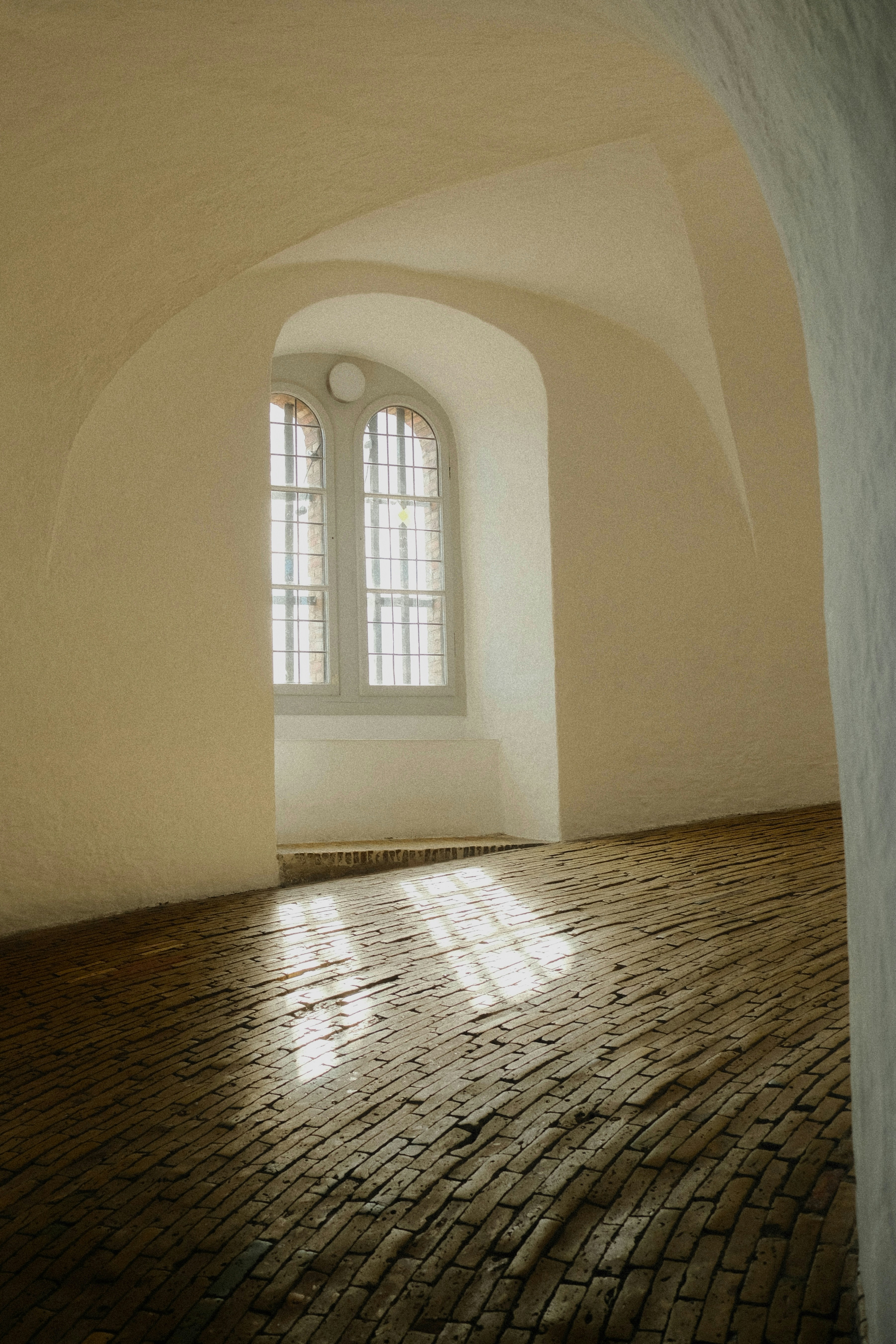 Sunlight through an arched window onto a rustic brick floor in a room