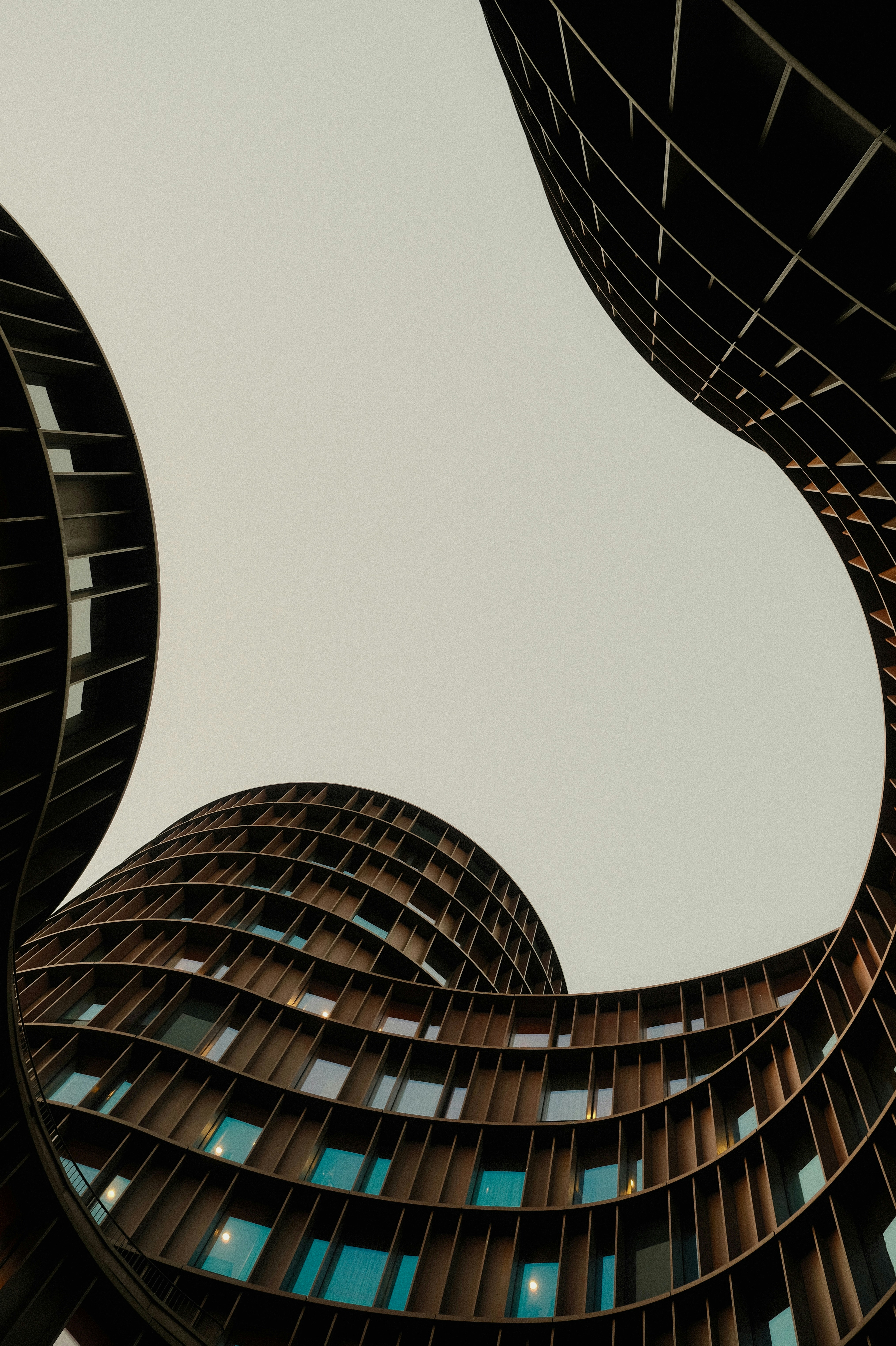 Curved modern buildings with dark grid facades framing a bright overcast sky