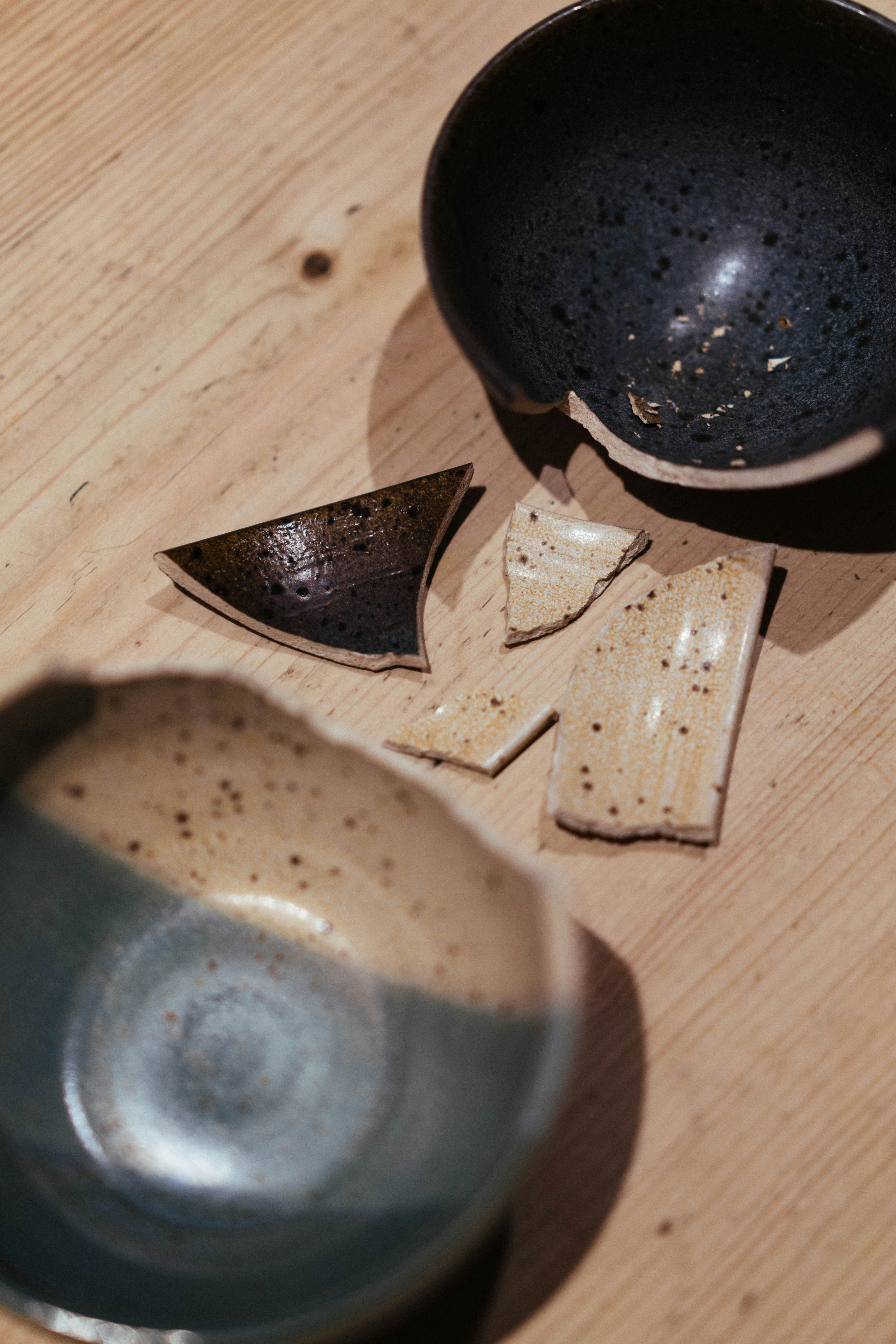 Broken ceramic bowls and scattered shards on a light wooden surface