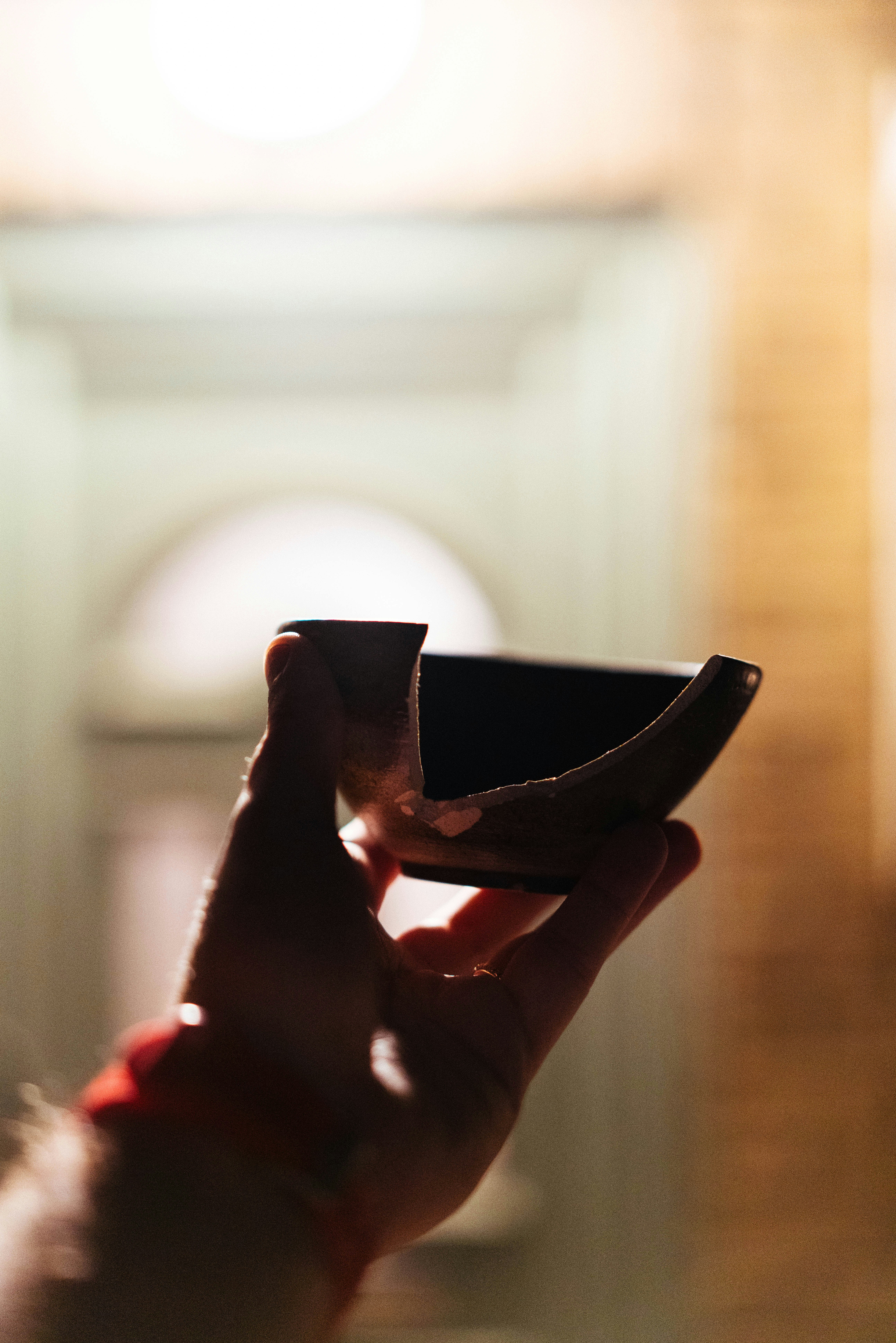 A hand holding a broken ceramic bowl against a blurred sunlit doorway