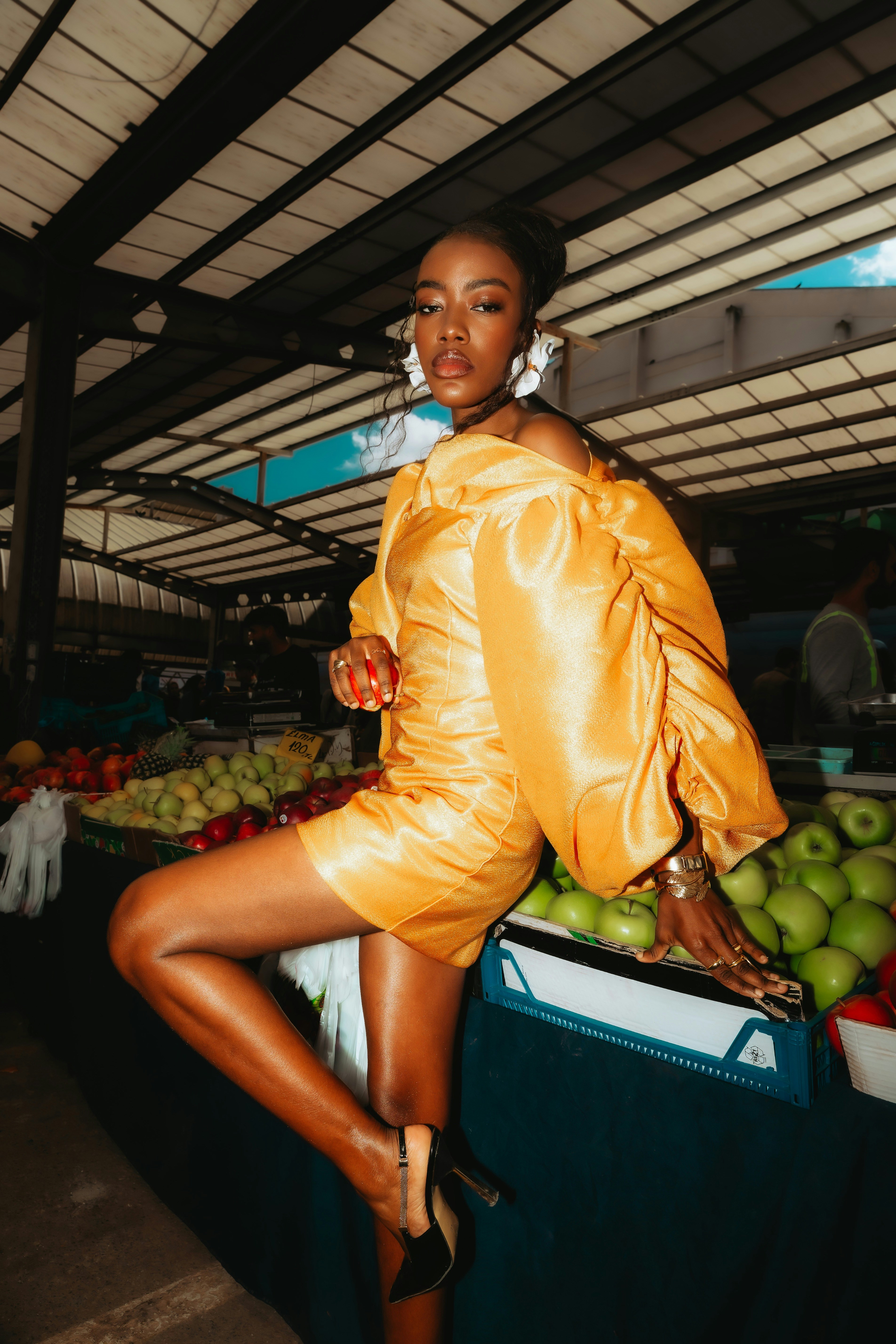 A woman in a yellow dress posing at a fruit market stall