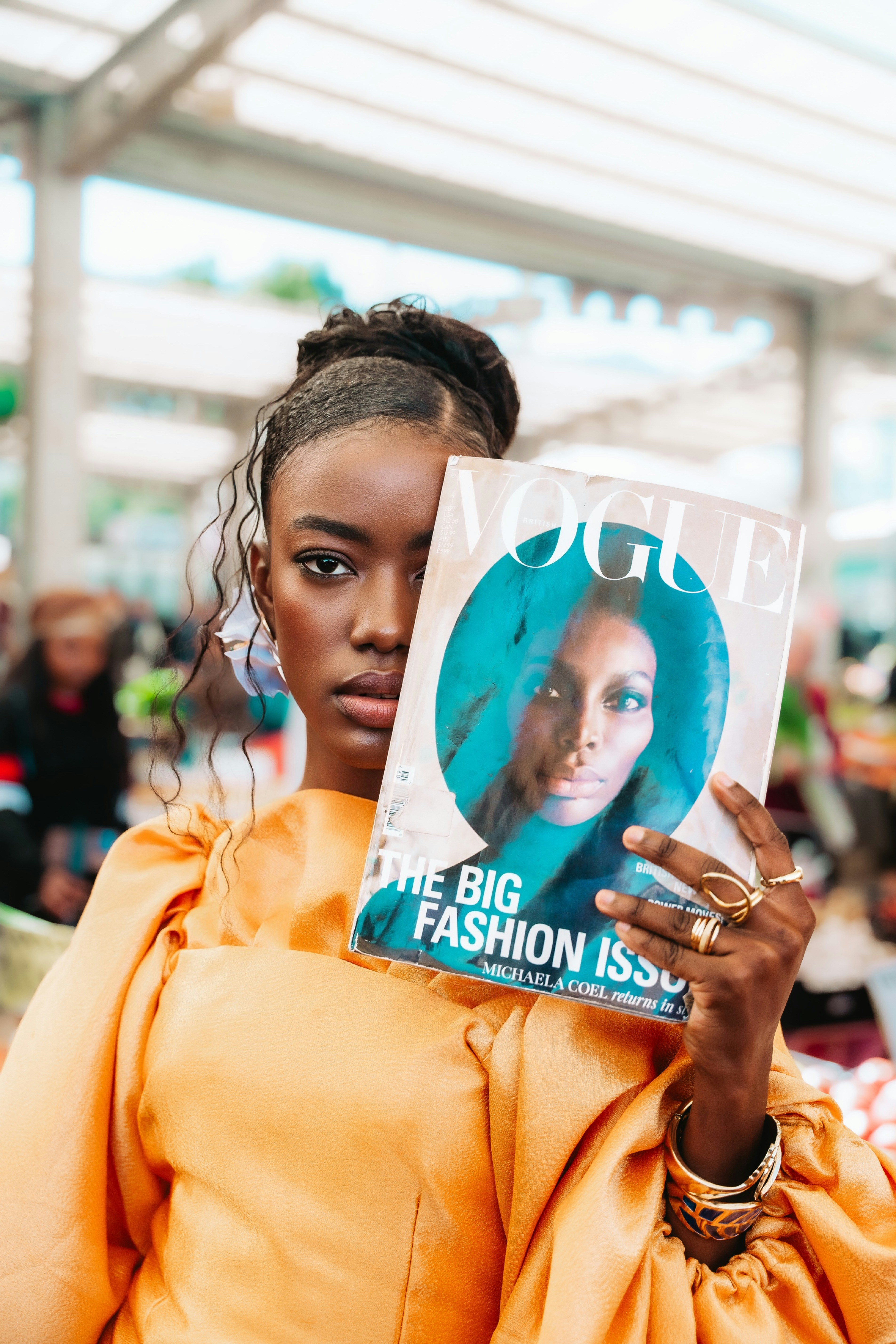 A woman in an orange top holding a fashion magazine over her face