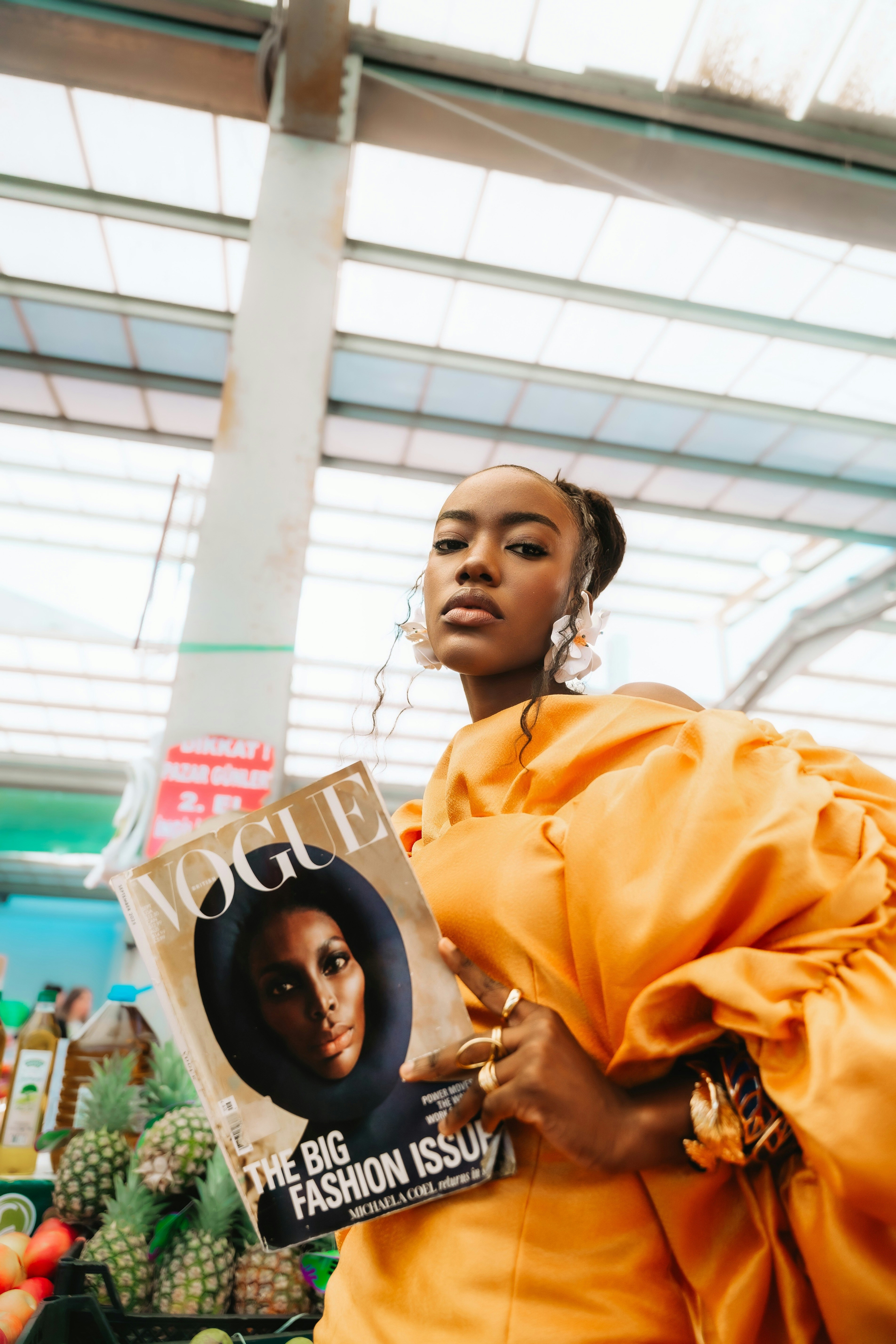 A woman in a yellow dress holding a fashion magazine in a market