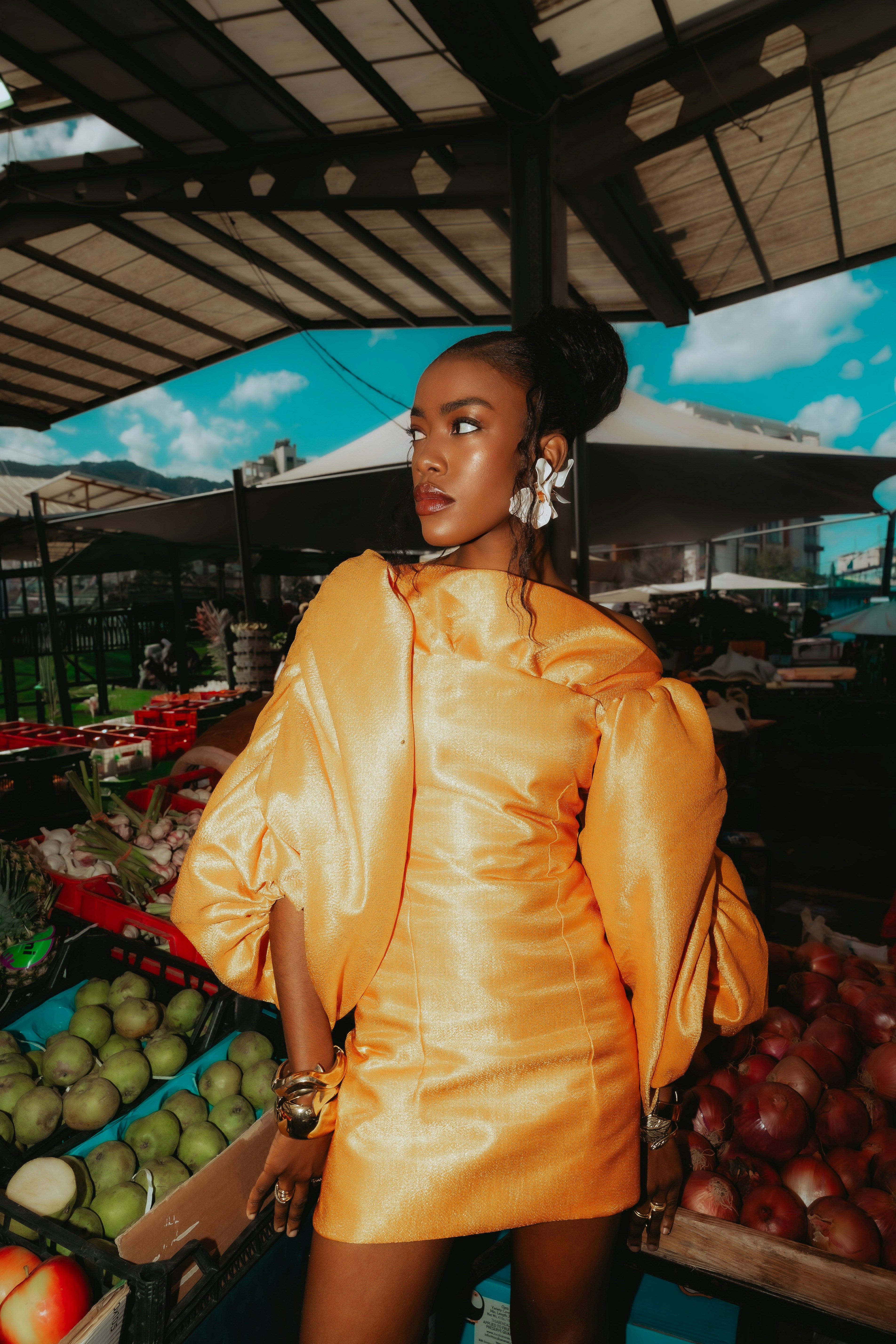 A woman in a bright orange dress standing at a produce market stall