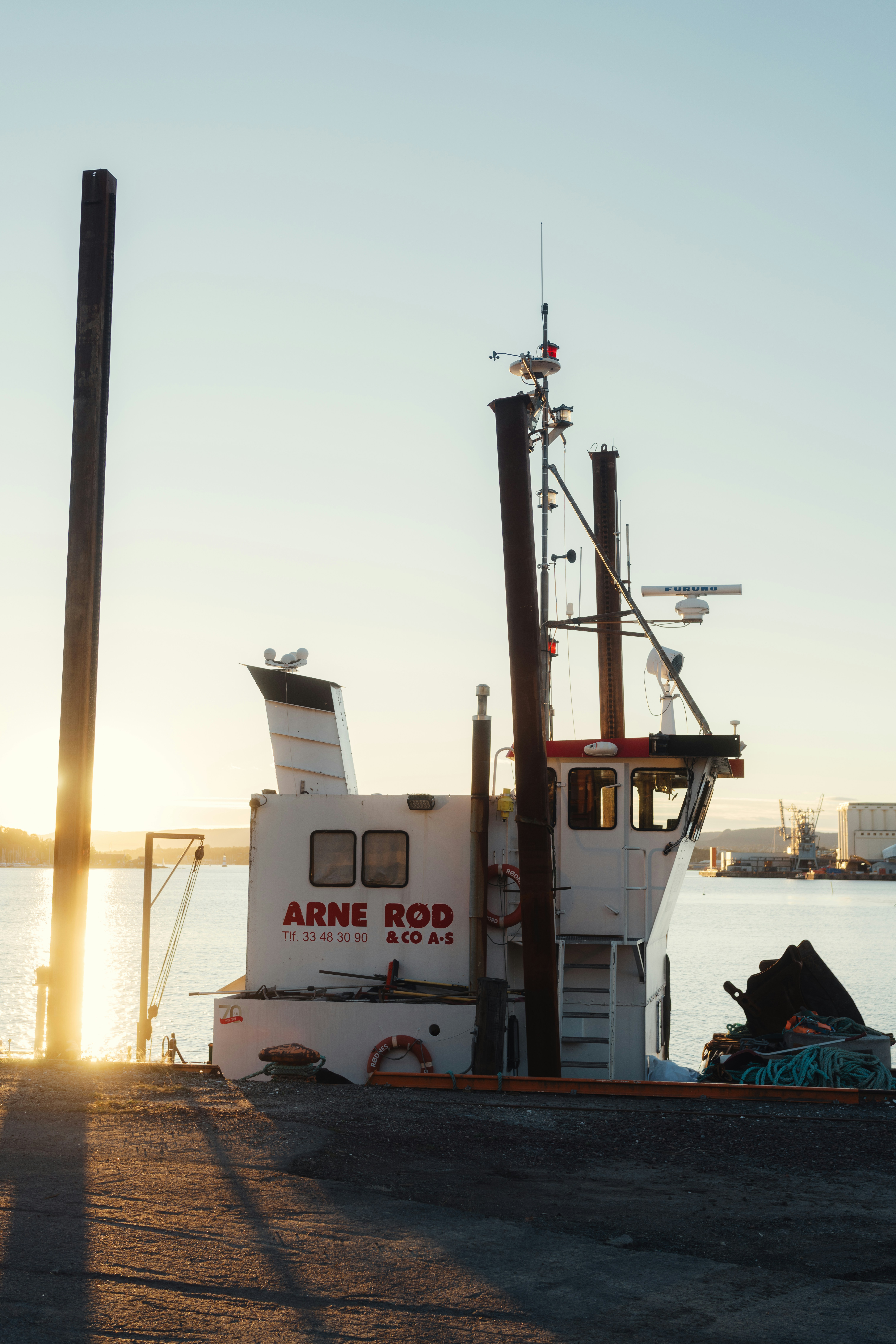 A white work boat docked in Oslo harbor during the golden hour