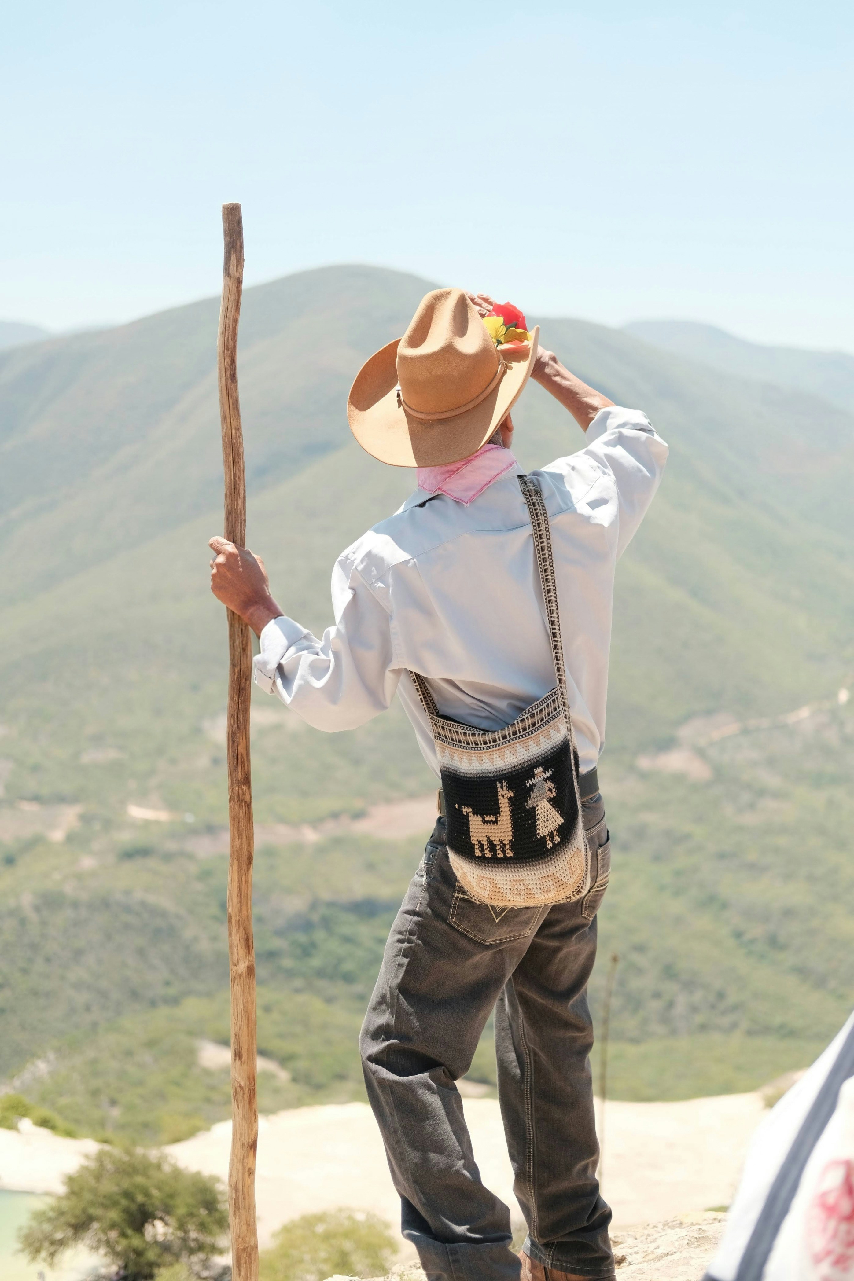 Una persona con sombrero vaquero y bolsa tejida mirando montañas verdes