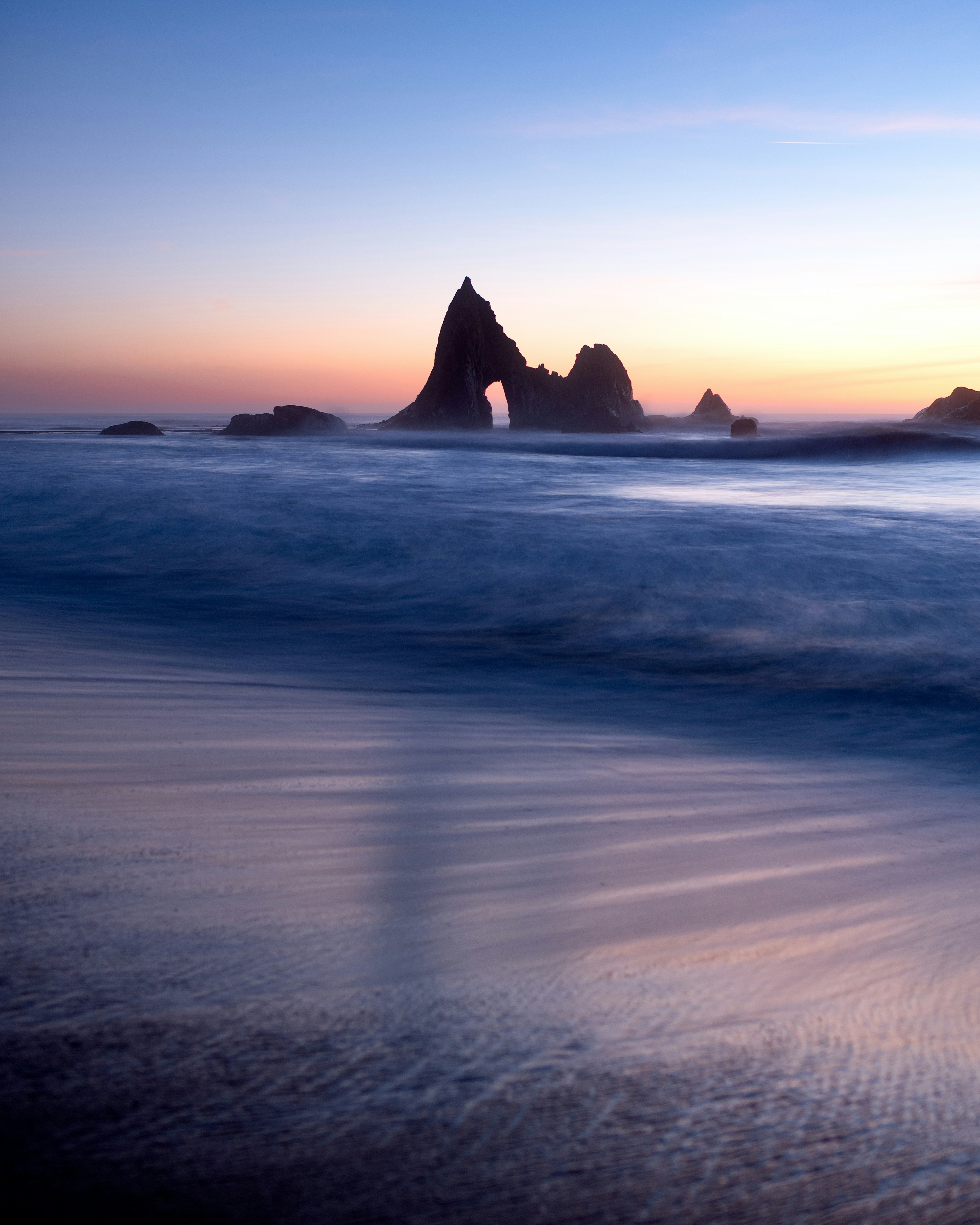 Sea stacks in the ocean under a soft orange and blue sky