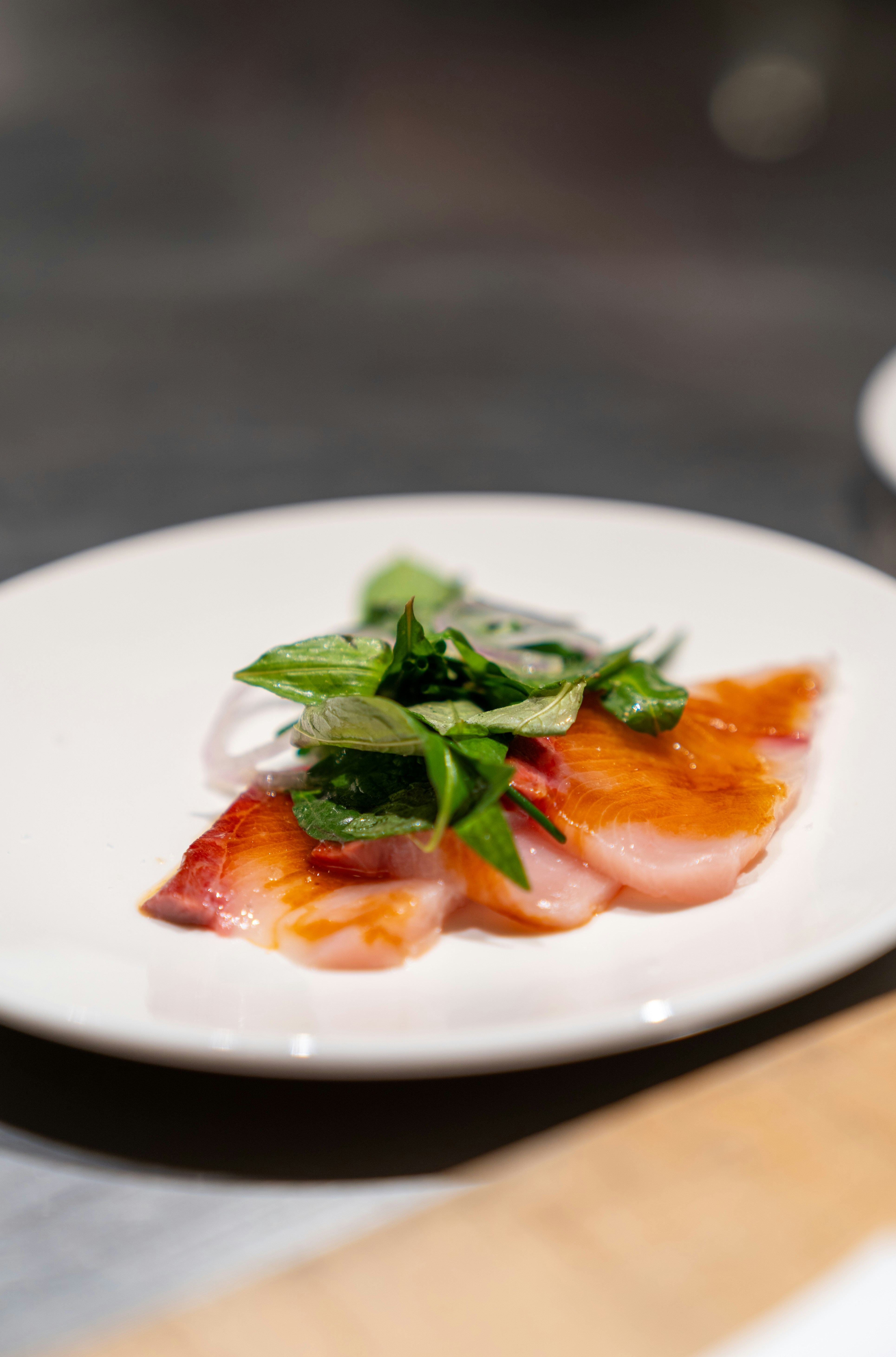 Thin slices of raw fish topped with fresh green herbs on a white plate