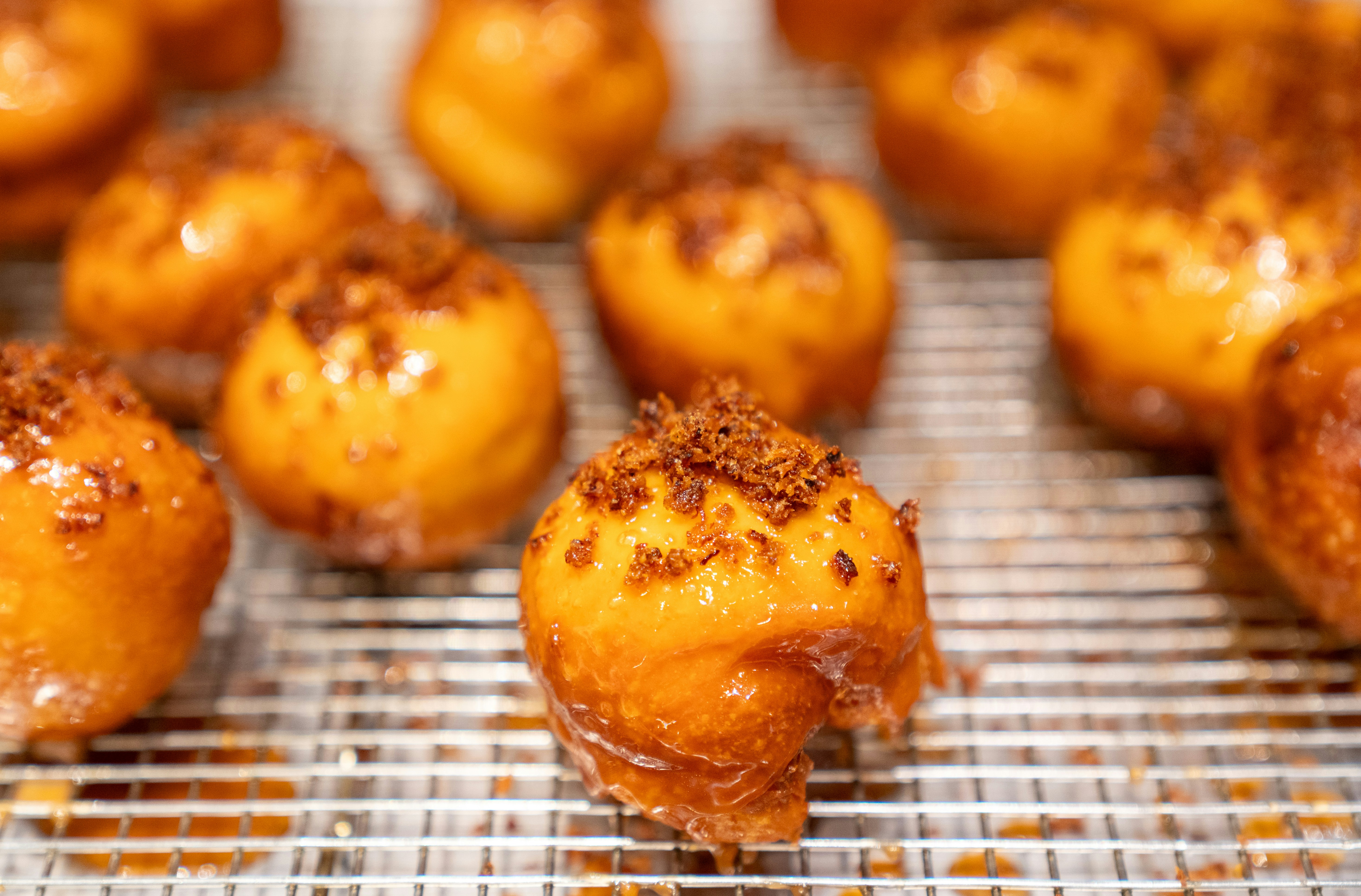 Glazed donut holes topped with brown sugar on a metal cooling rack