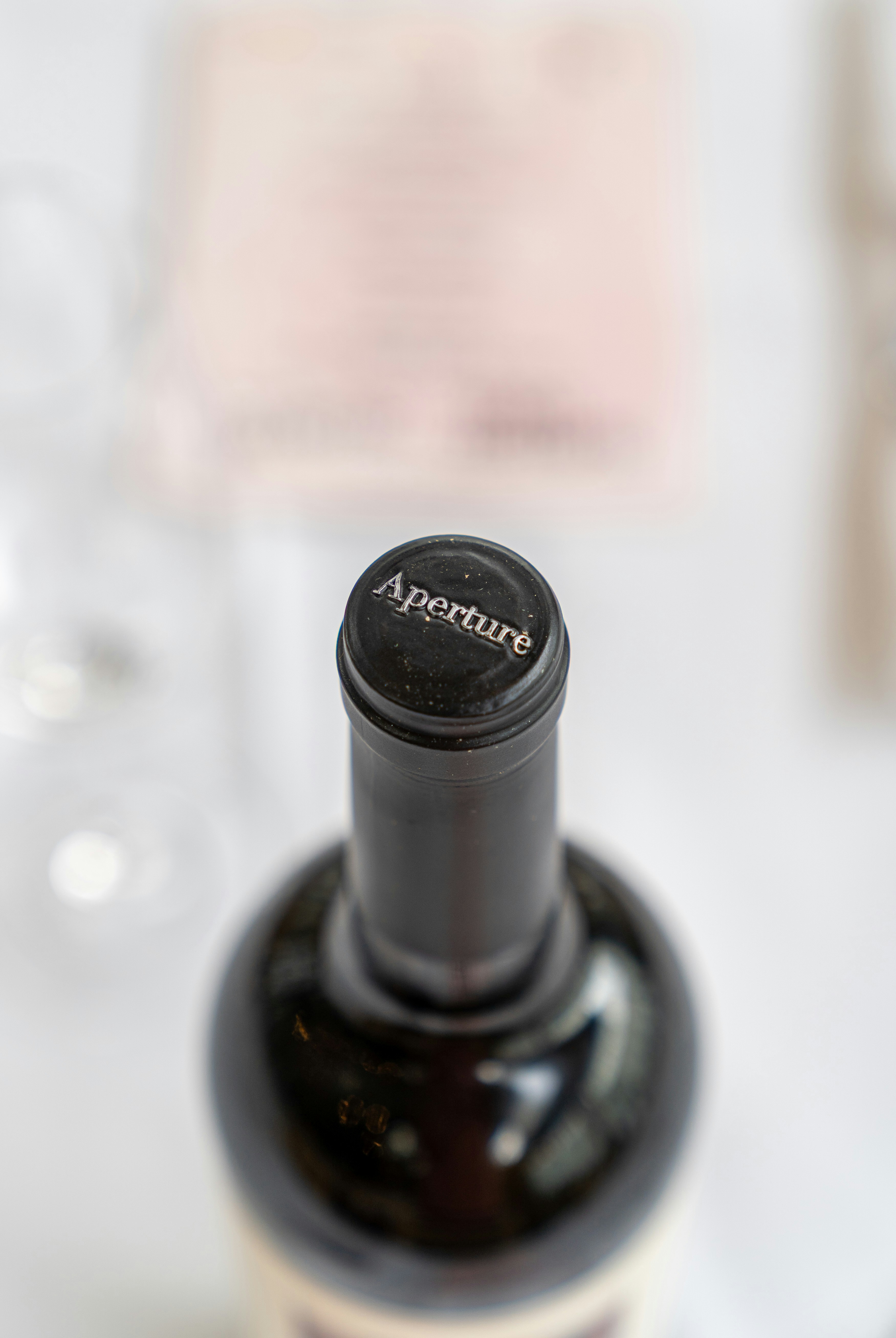 A wine bottle neck with a black cap embossed with the word Aperture