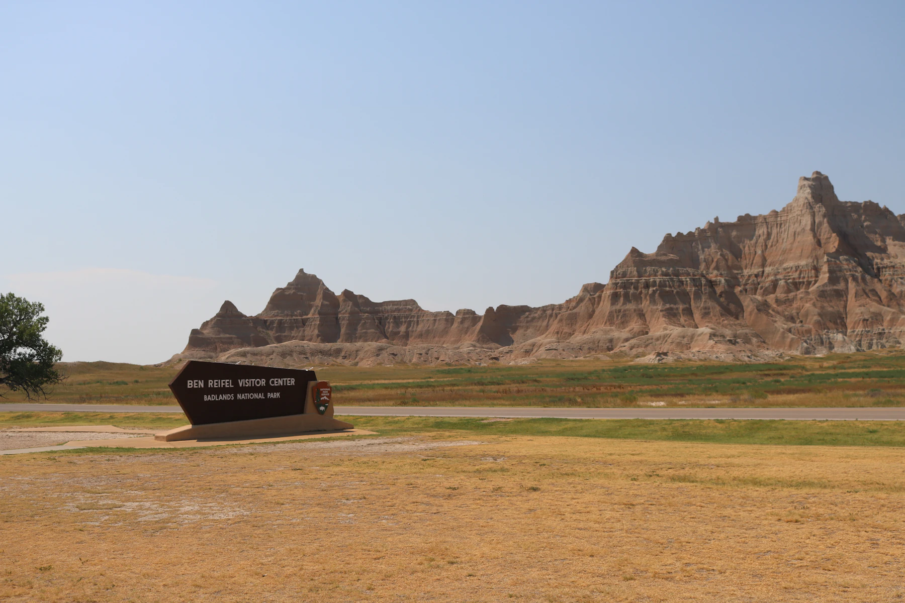 The Ben Reifel Visitor Center sign beside a road, with the banded Badlands formations behind it