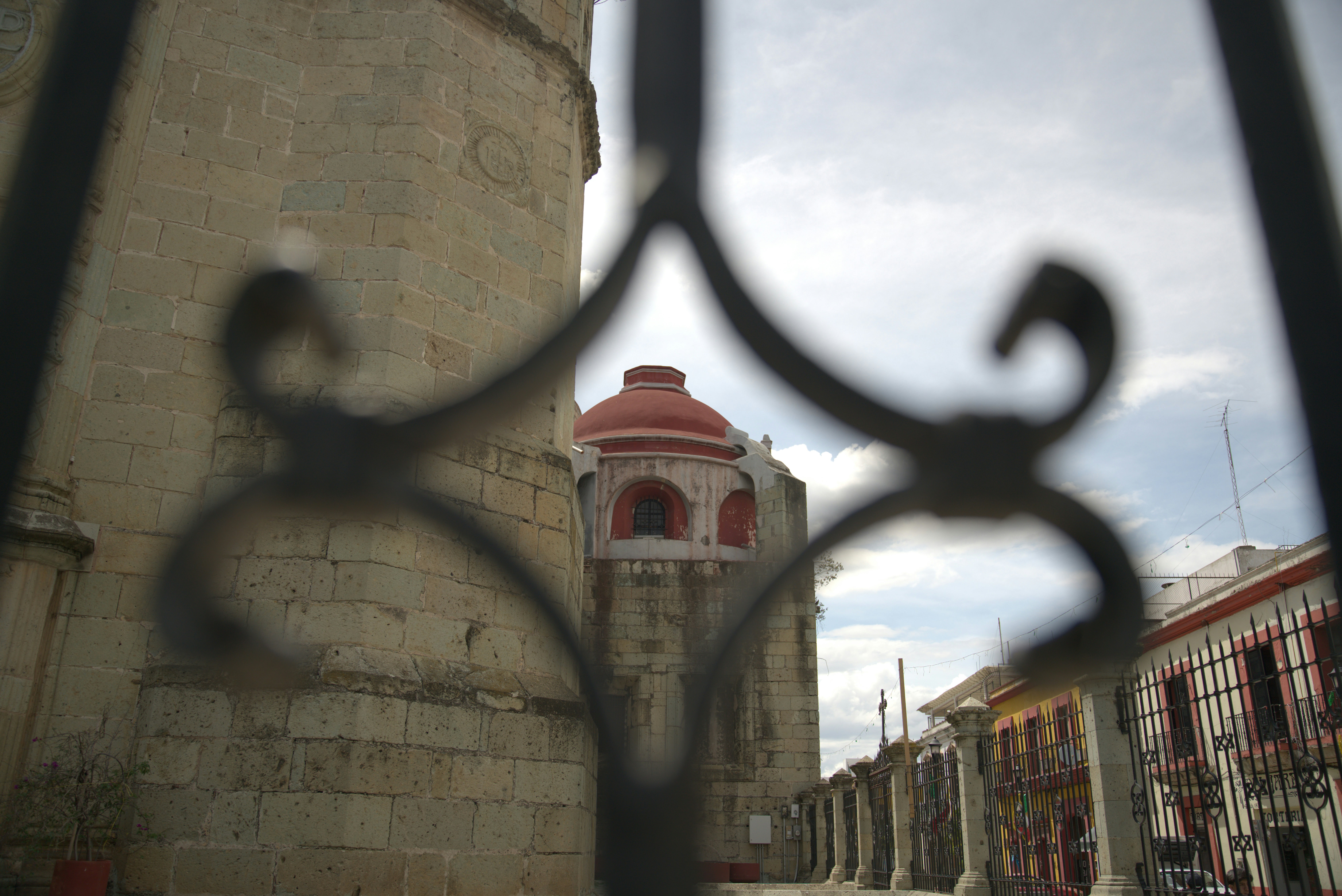 A stone church with a red dome viewed through a decorative iron fence