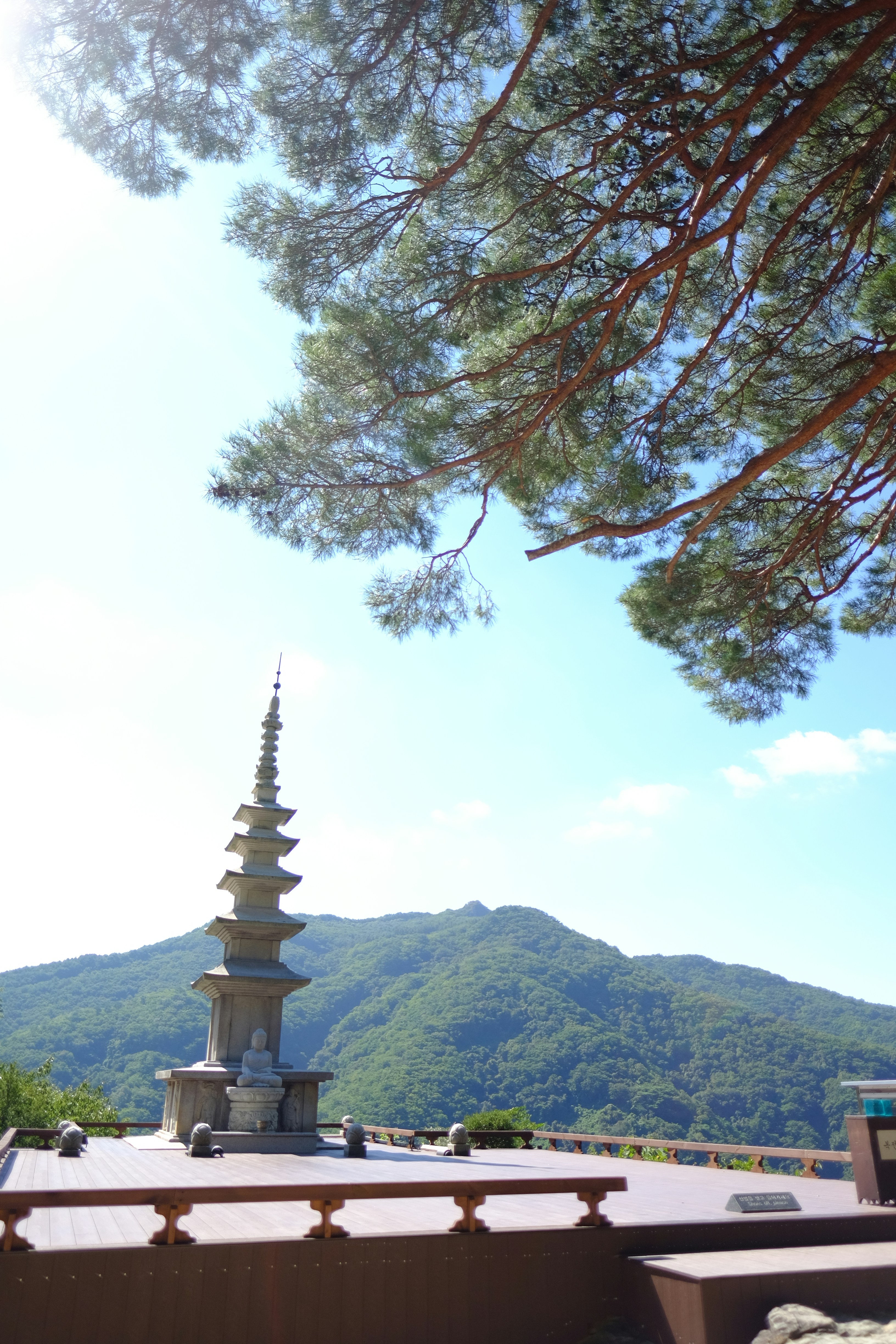 A stone pagoda with a small Buddha statue on a wooden deck overlooking mountains