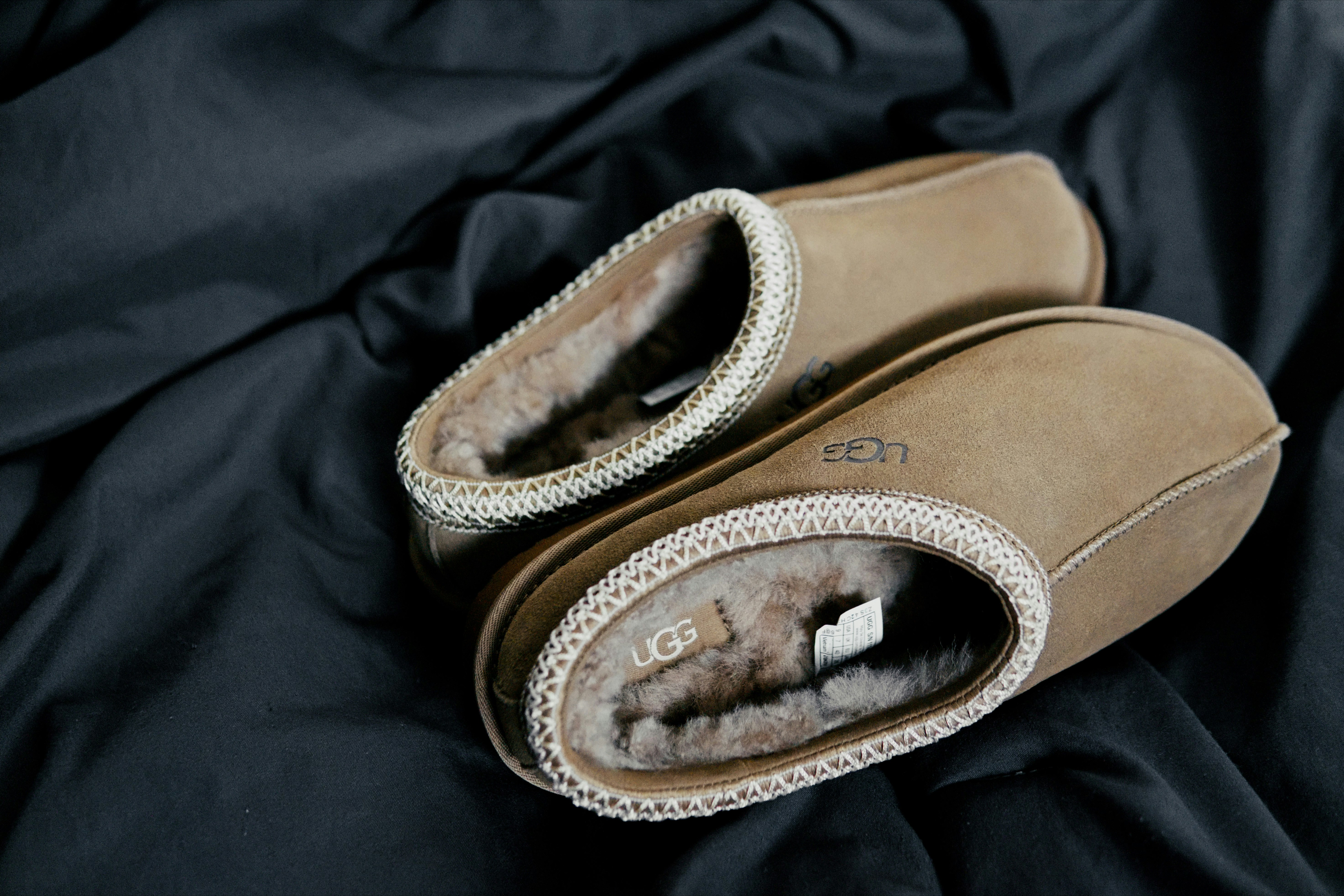 Two brown suede slippers with fur lining on a dark fabric surface