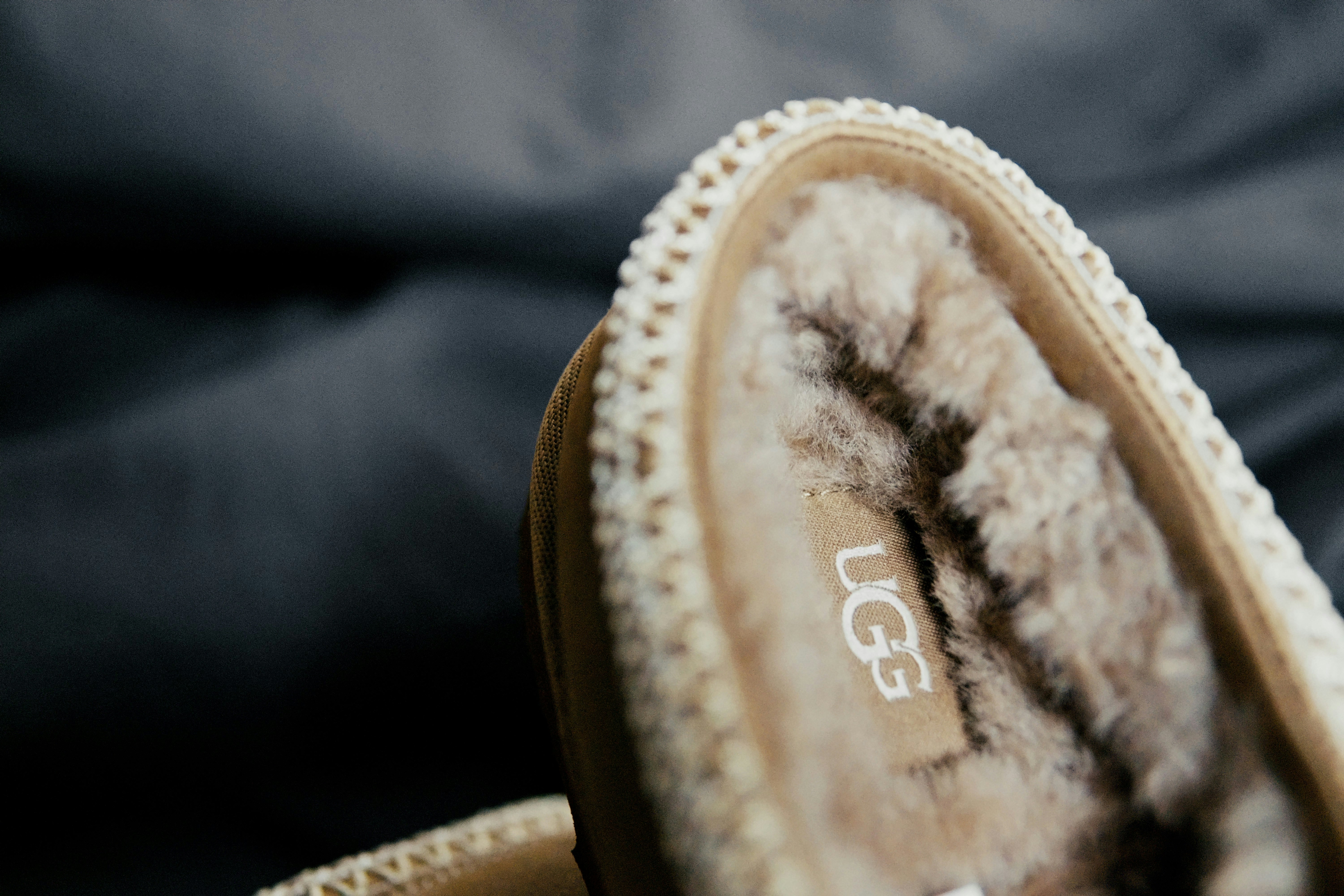 A tan suede slipper with a plush faux fur lining on a dark surface