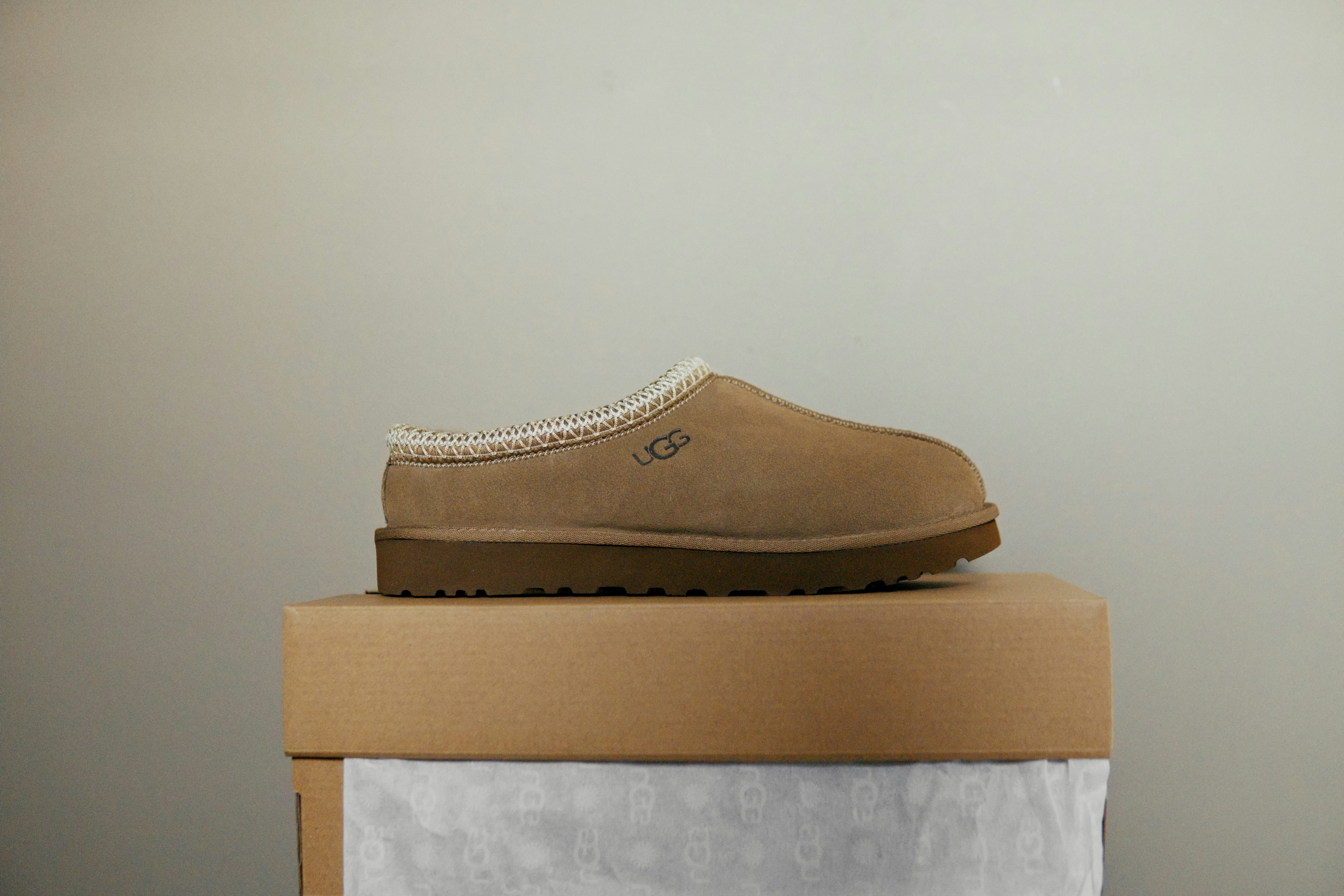A tan suede slipper with a braided trim on a cardboard box