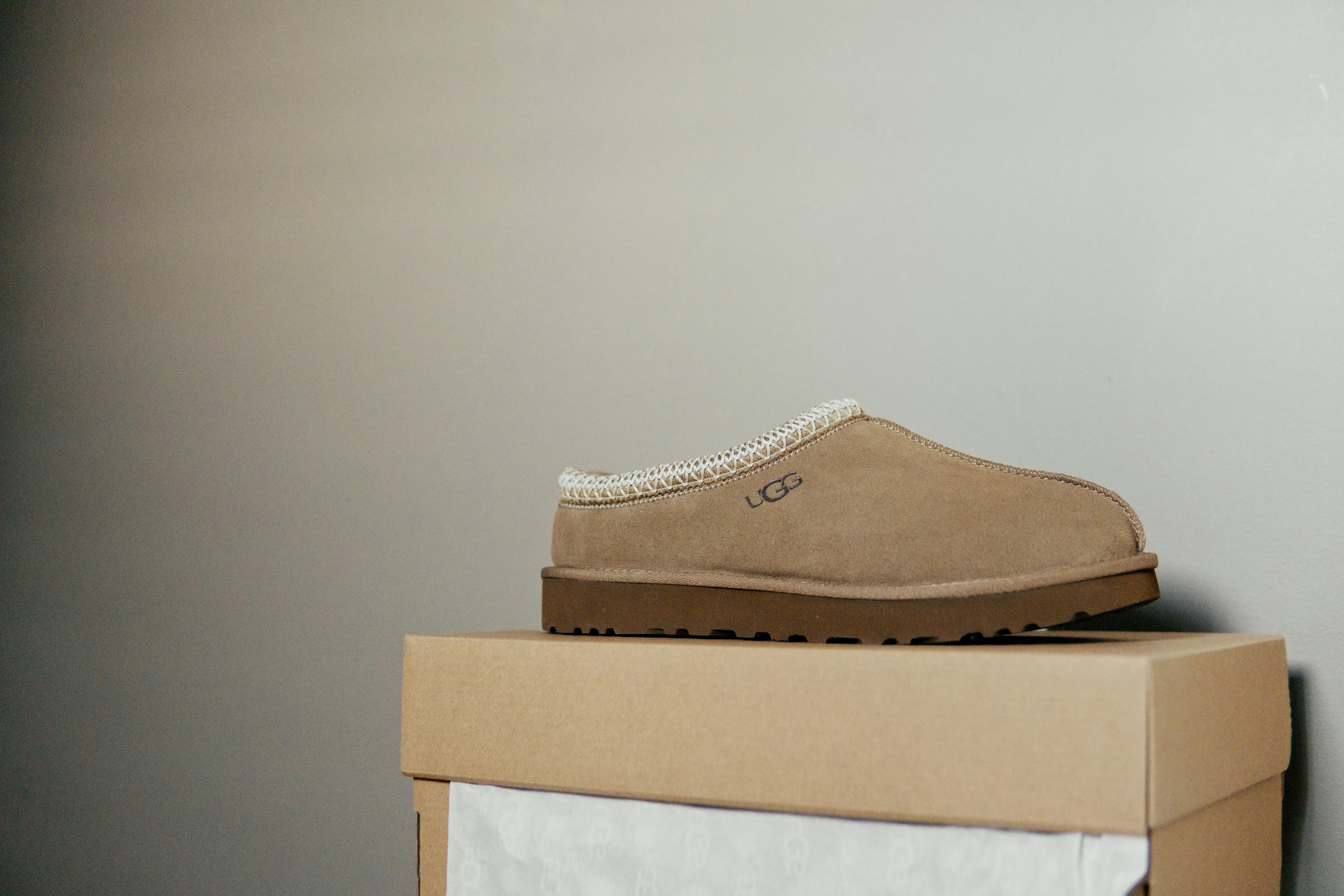 A tan suede slipper with a white stitched collar on a cardboard box