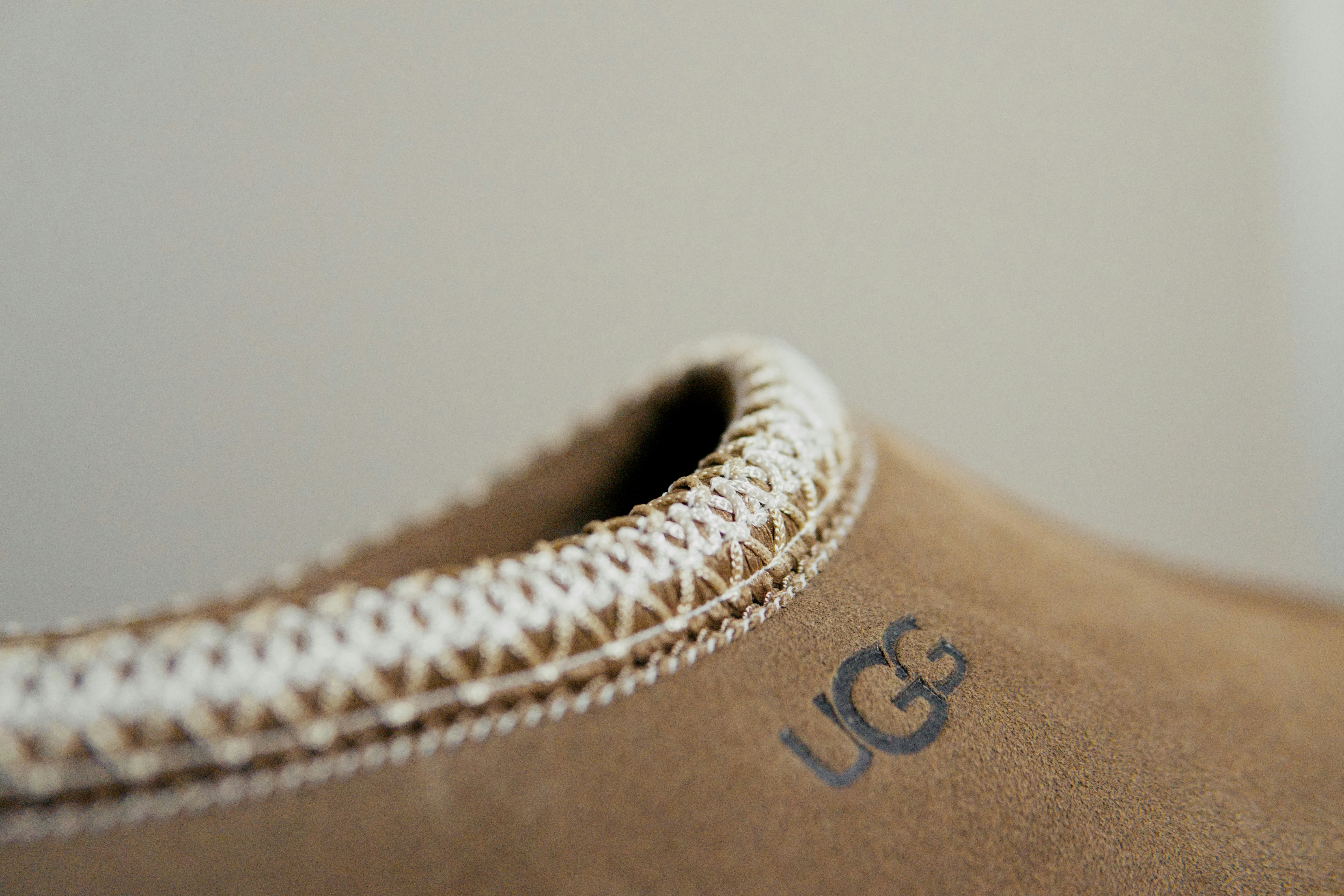 A brown suede slipper with a woven trim and a visible brand logo