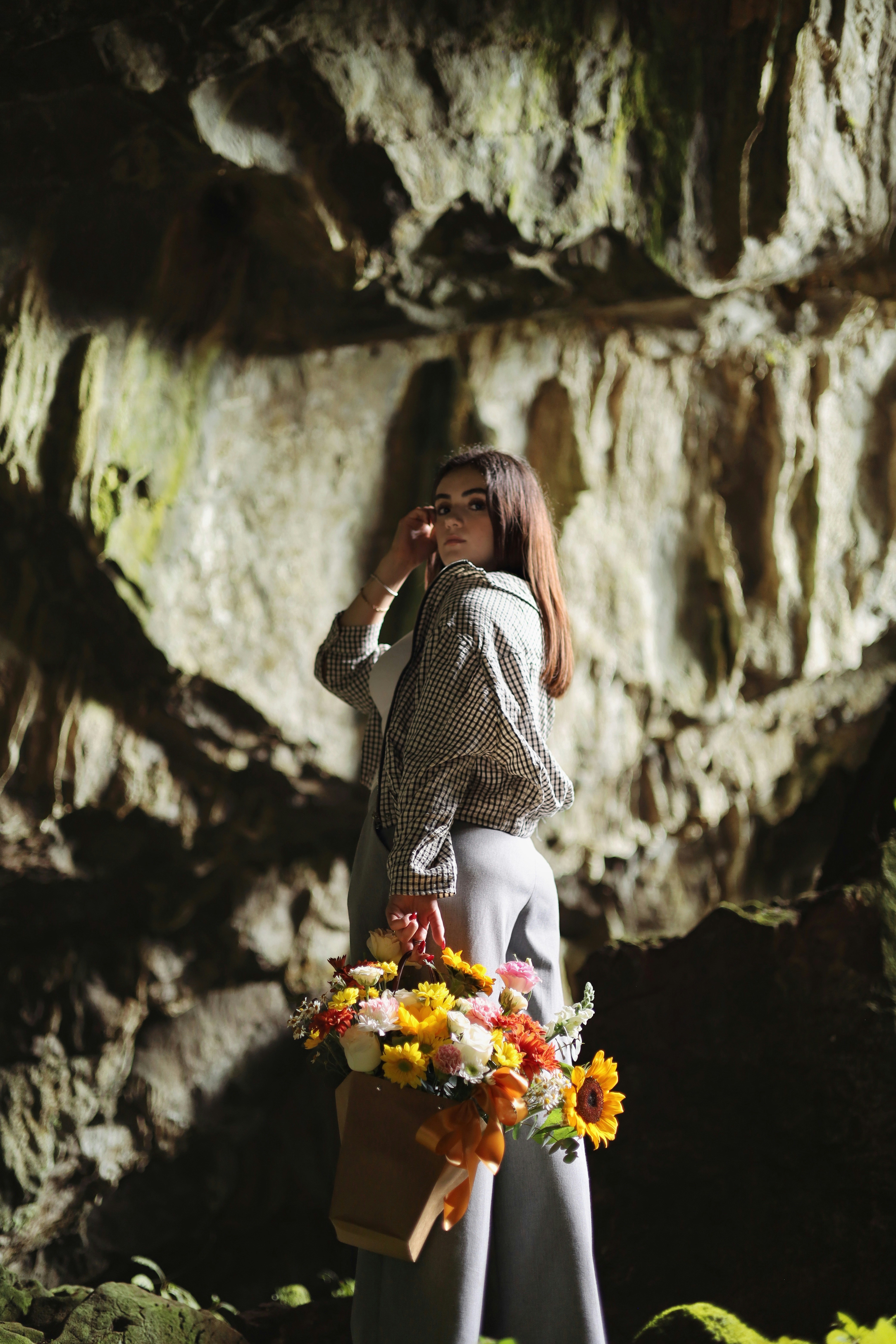 A woman in a plaid jacket holding a flower bouquet inside a cave