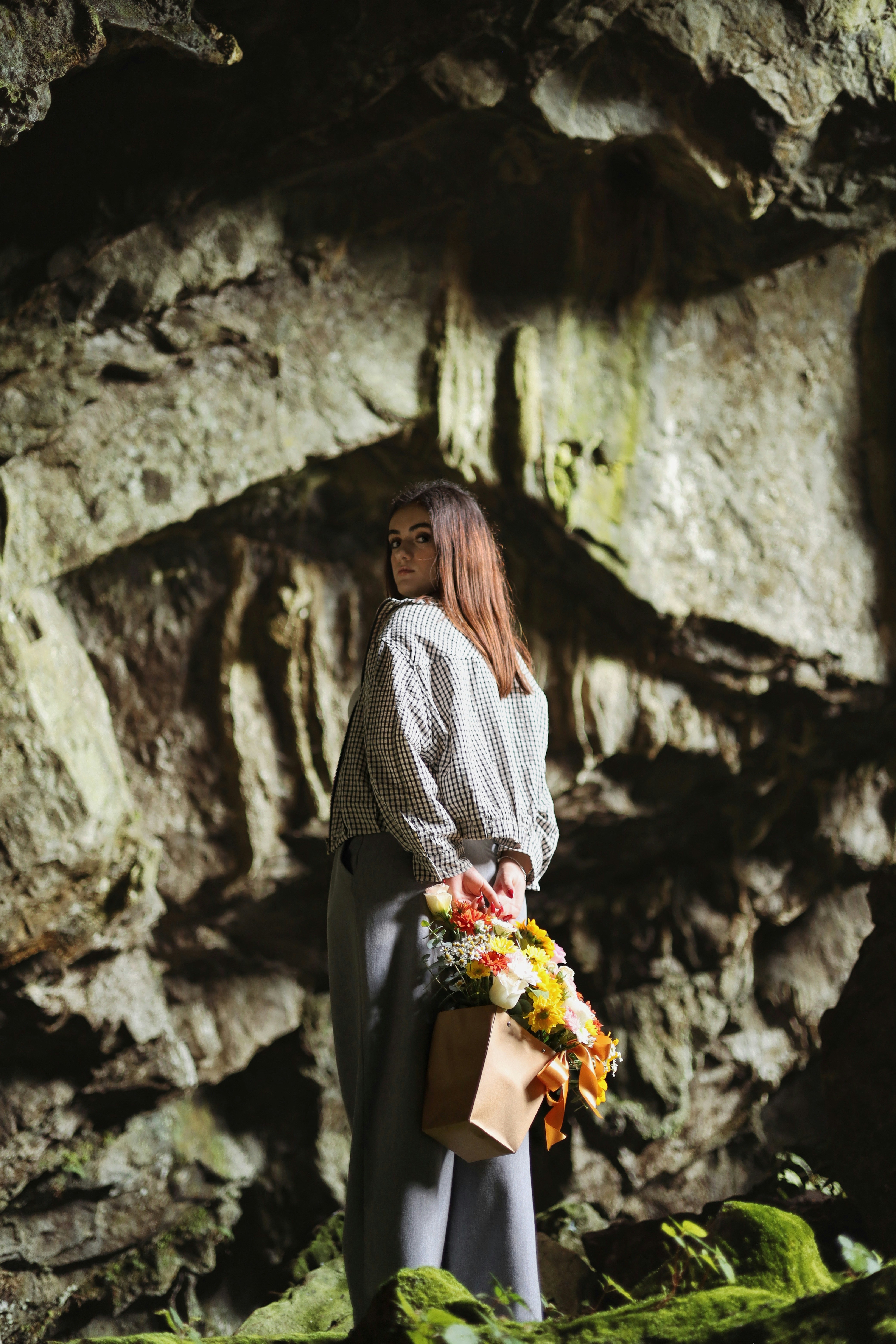Una donna che tiene un mazzo di fiori dentro una grotta rocciosa